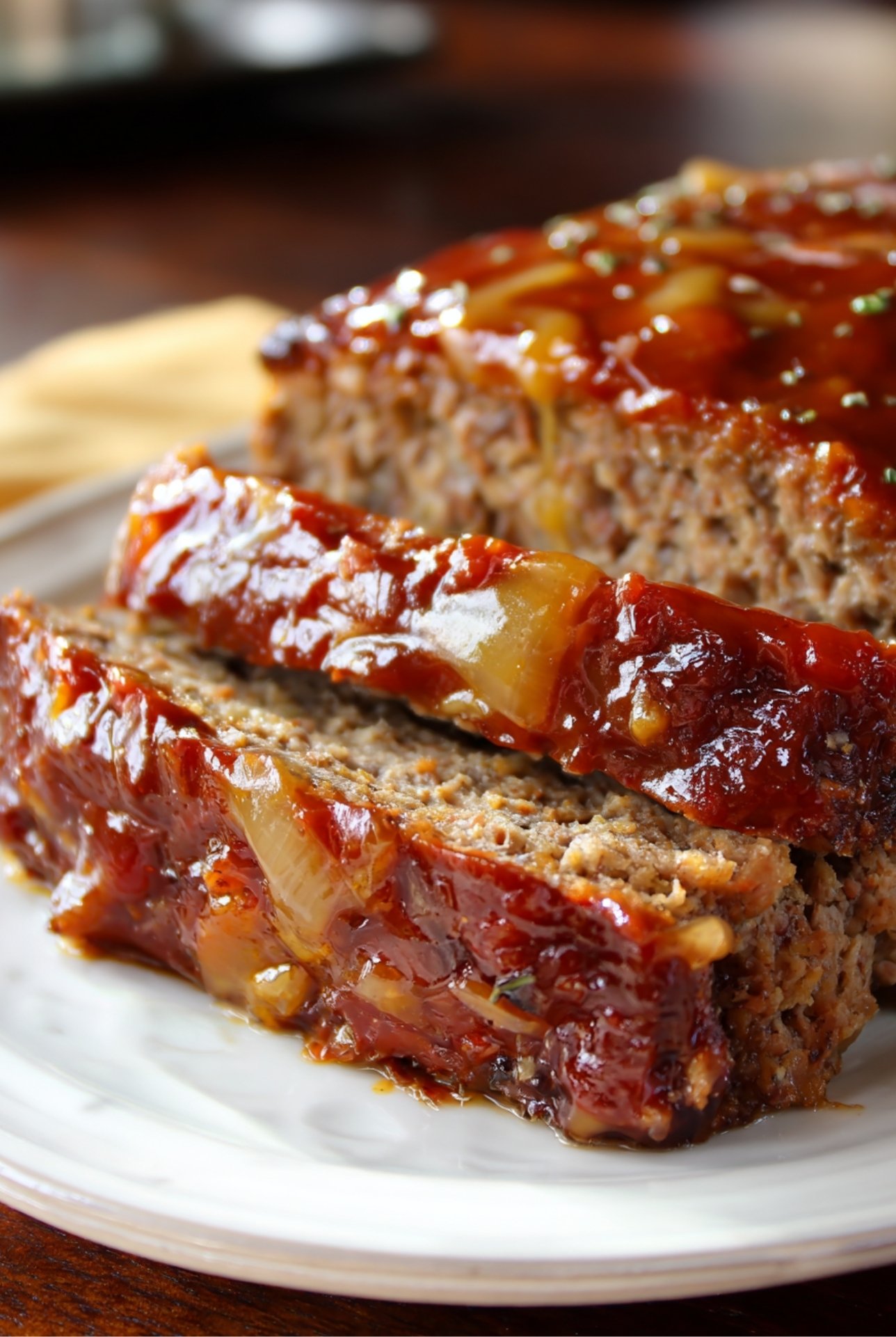 Classic meatloaf topped with sweet mustard glaze and onions, sliced and served for dinner.