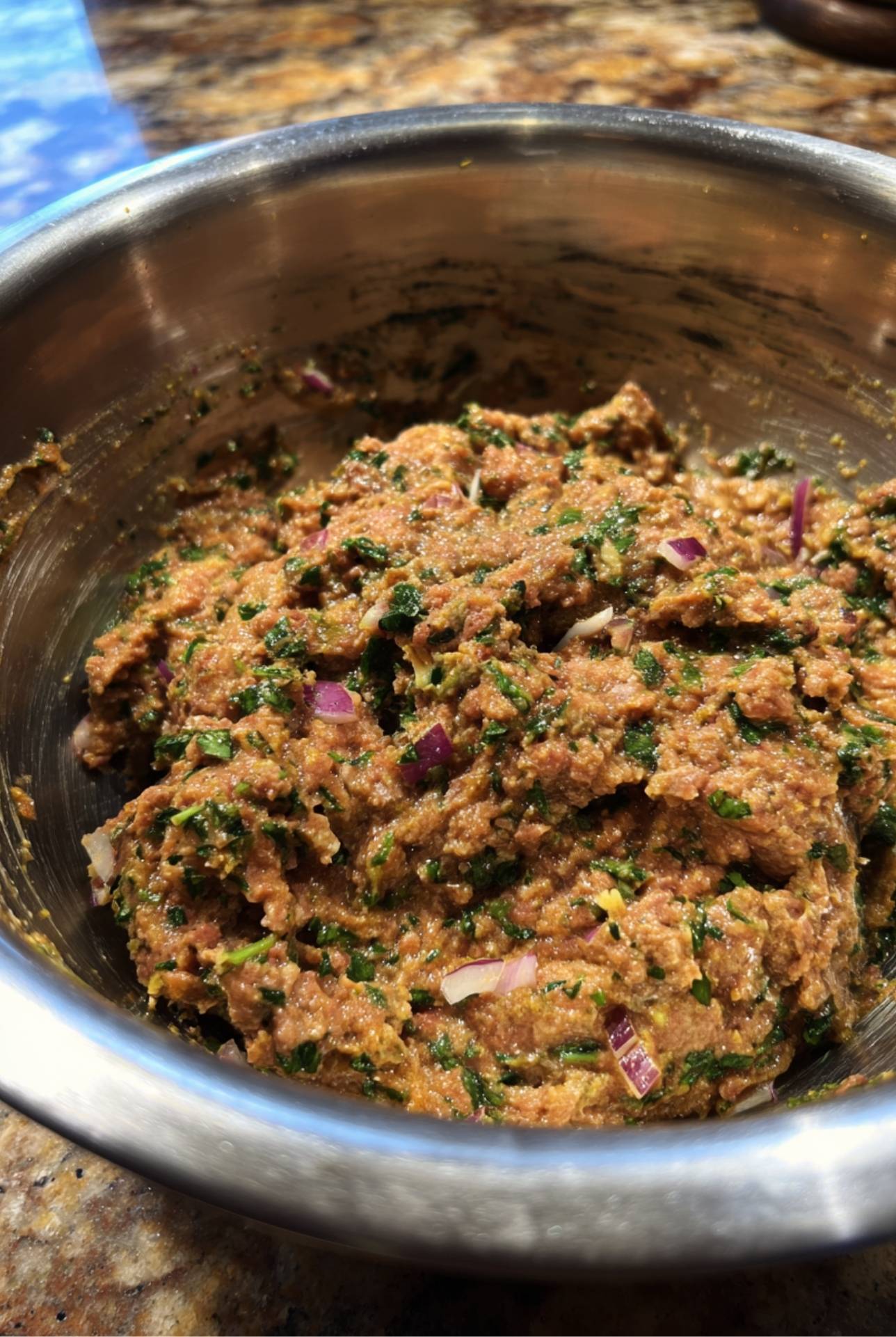 Seasoned ground lamb mixture with fresh parsley and onion in a stainless steel mixing bowl