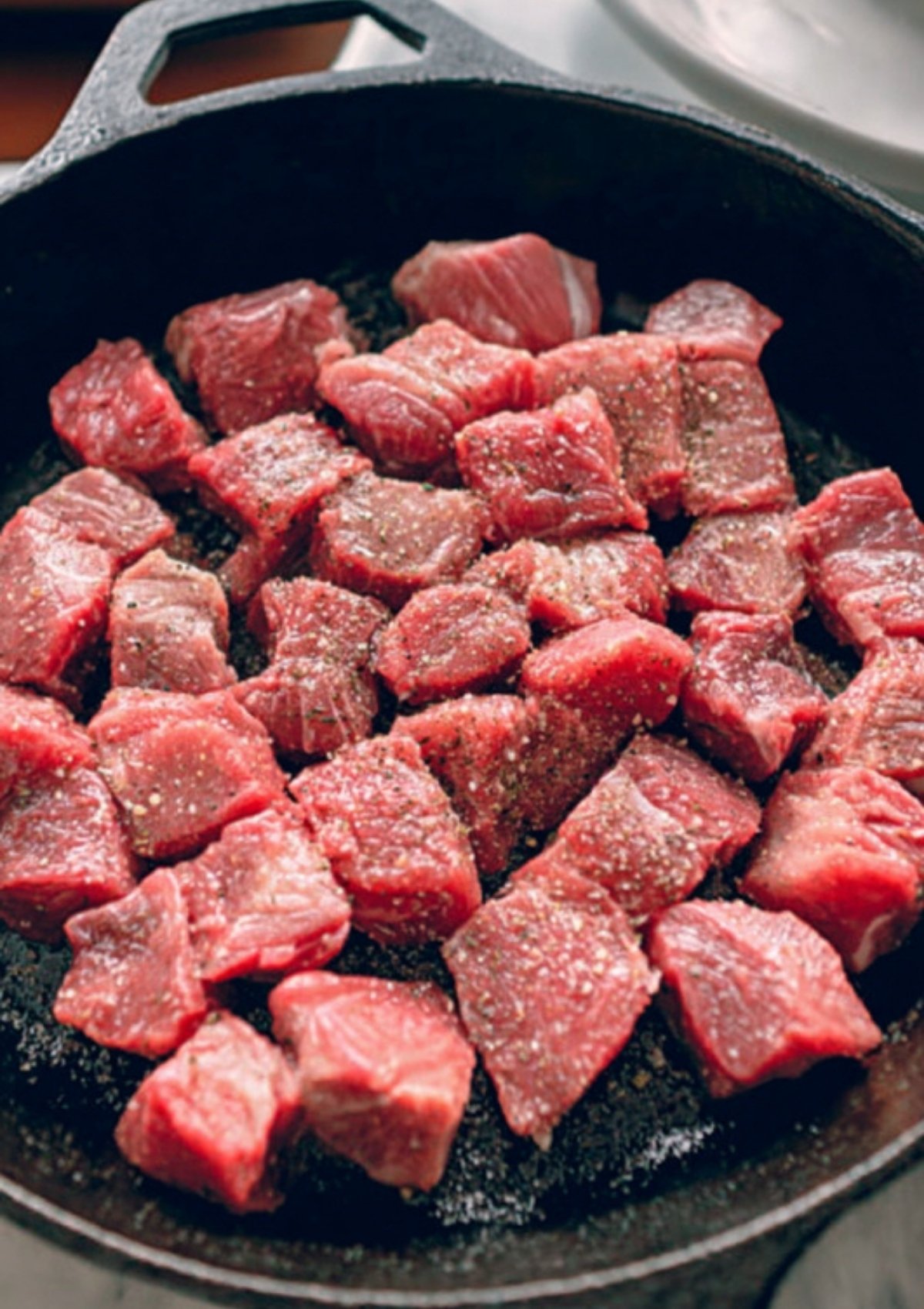 Raw steak cubes in a cast iron skillet sprinkled with salt and pepper, ready to be seared for garlic butter steak bites.