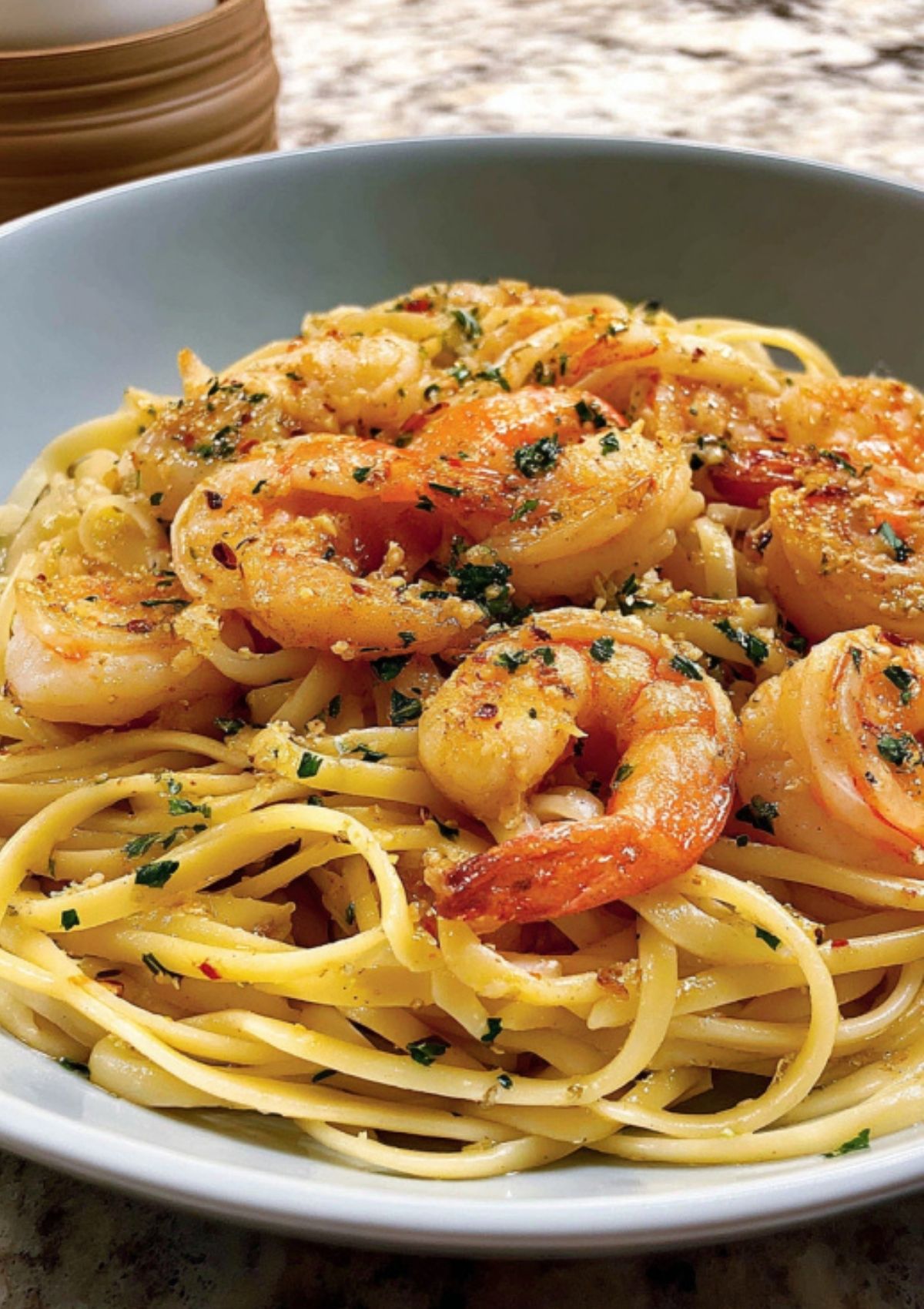Close-up of shrimp scampi with linguine pasta in a white bowl, featuring juicy shrimp, fresh parsley, red pepper flakes, and a glossy lemon garlic butter sauce.