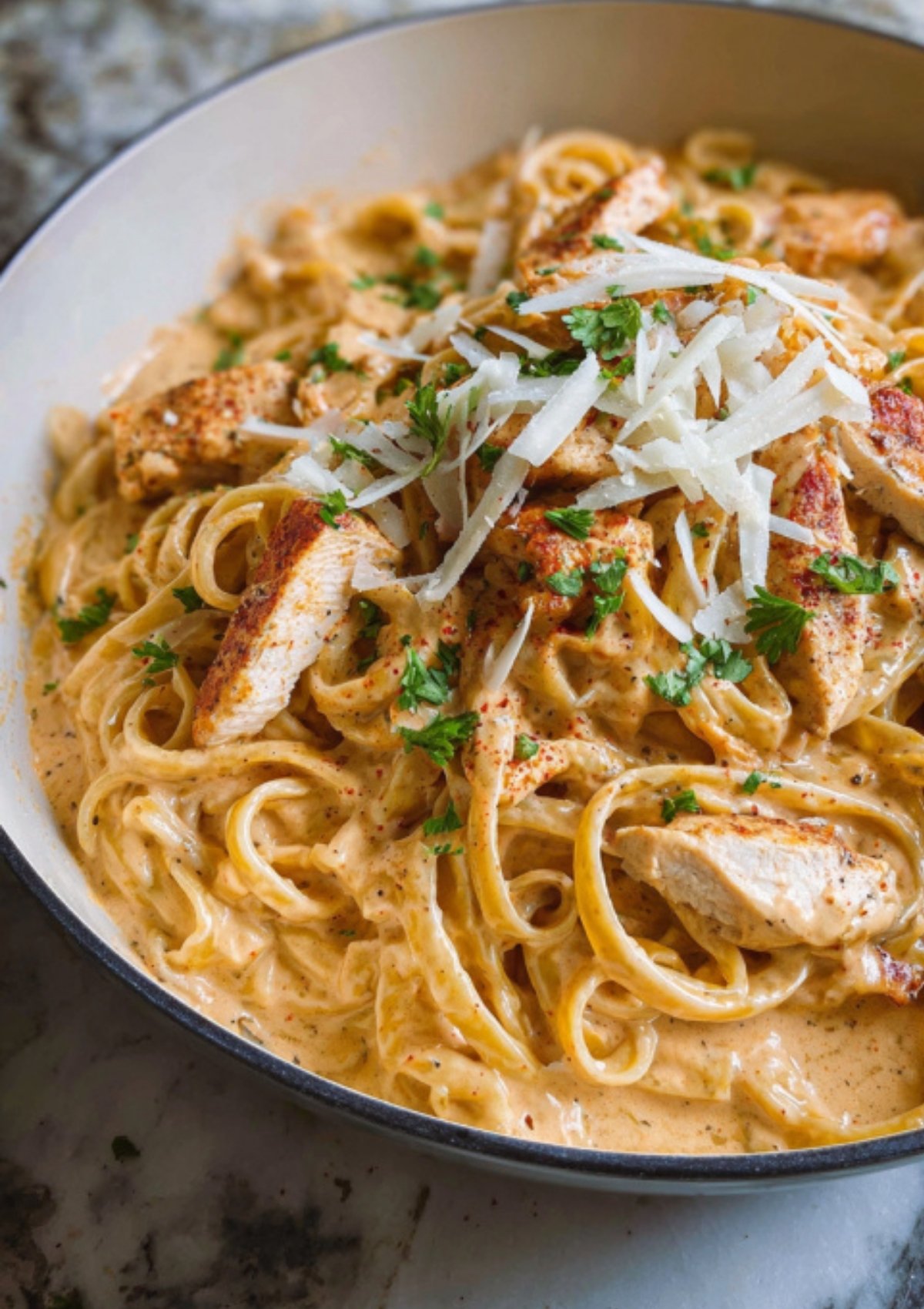 Creamy Cajun chicken Alfredo topped with grated parmesan cheese and chopped parsley in a white skillet.