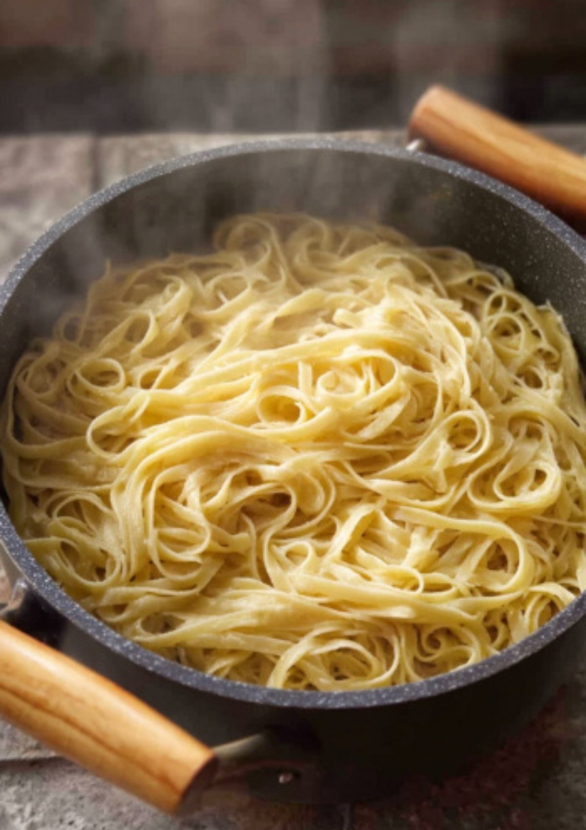 Fettuccine pasta boiling in a pot with steam rising, ready for creamy Alfredo sauce.