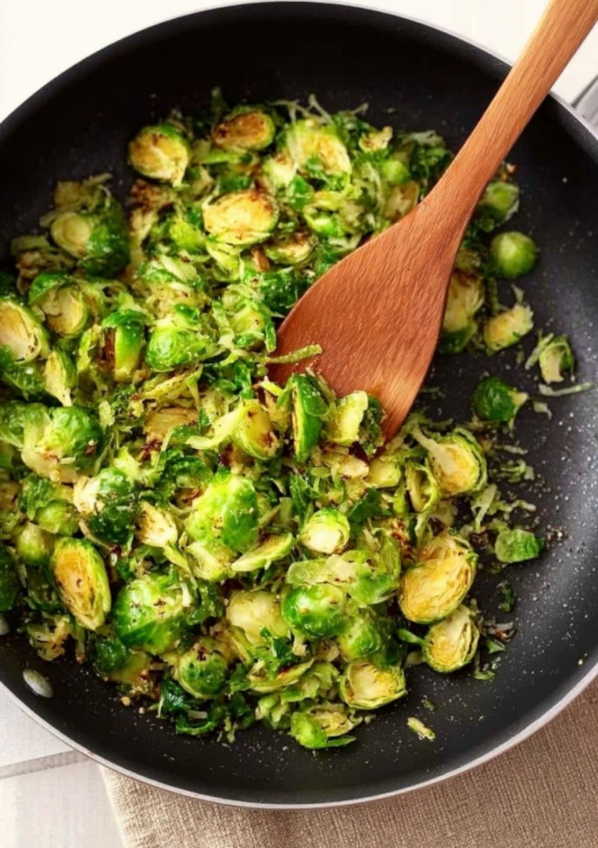 Brussels sprouts sautéing in a skillet with garlic and olive oil, stirred with a wooden spoon for pizza topping.