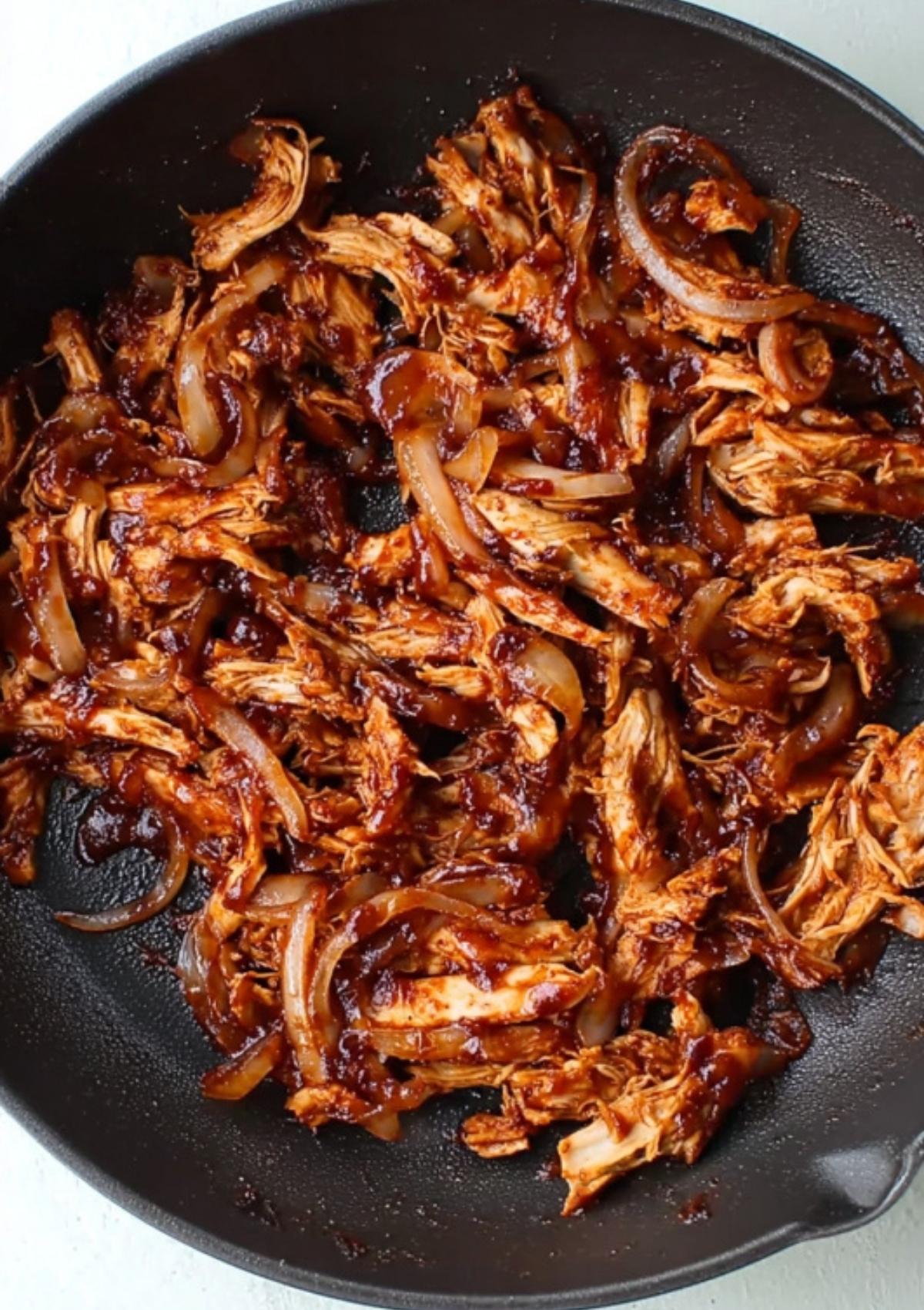 Juicy BBQ chicken and onions sizzling together in a pan, coated in smoky sauce.