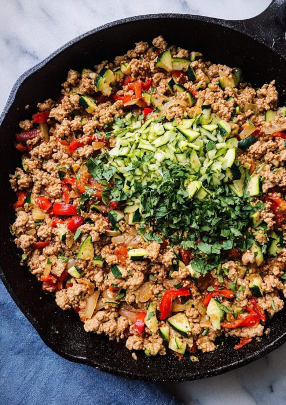 Ground turkey, bell peppers, and onions in a skillet with chopped zucchini and fresh cilantro added for color and flavor.