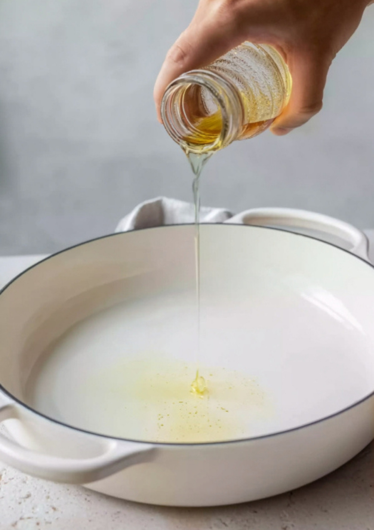 Hand pouring oil into a white skillet before cooking teriyaki chicken.