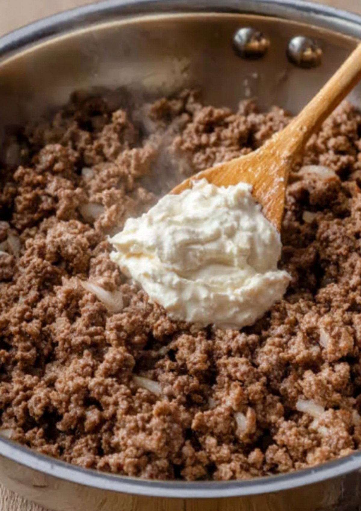 Wooden spoon stirring mayonnaise into cooked ground beef for extra juicy cheeseburger sliders.