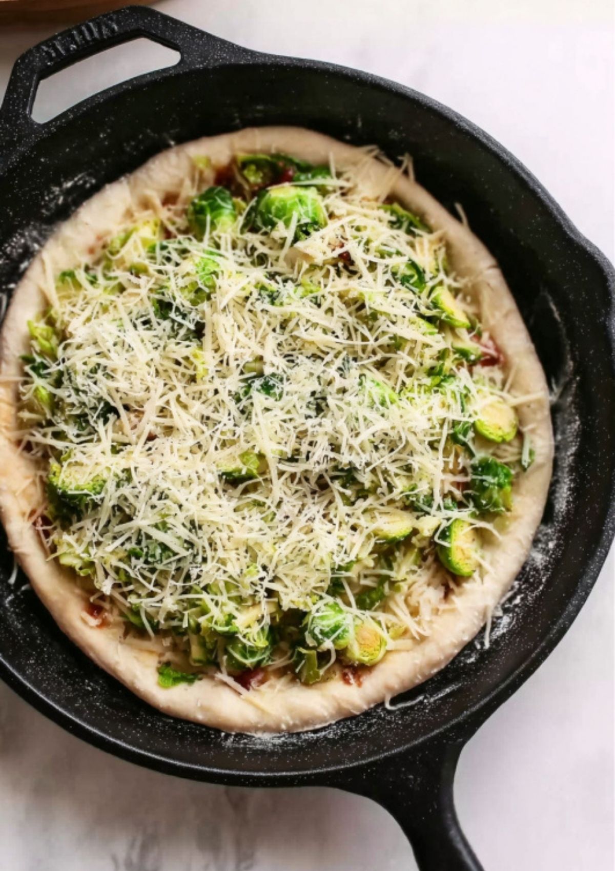 Brussels sprouts and grated cheese layered over pizza crust in a cast iron pan before baking.