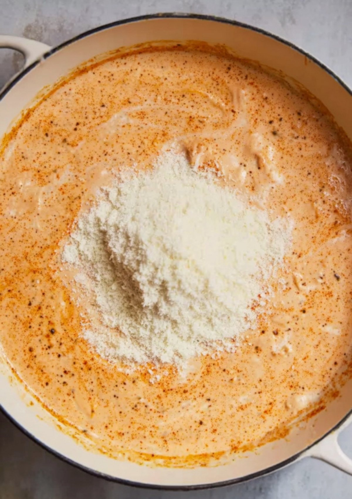 Grated parmesan melting into a creamy Cajun Alfredo sauce in a skillet, making it rich and smooth.