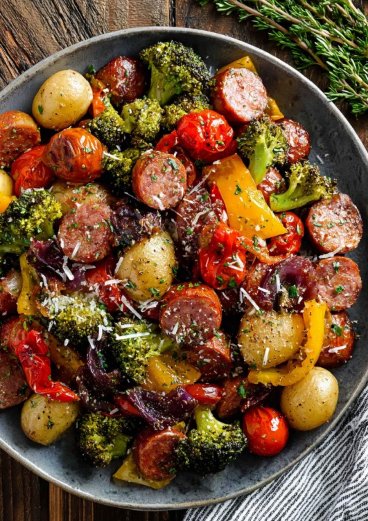 Close-up of roasted sausage, broccoli, tomatoes, bell peppers, and potatoes topped with parmesan cheese and herbs.