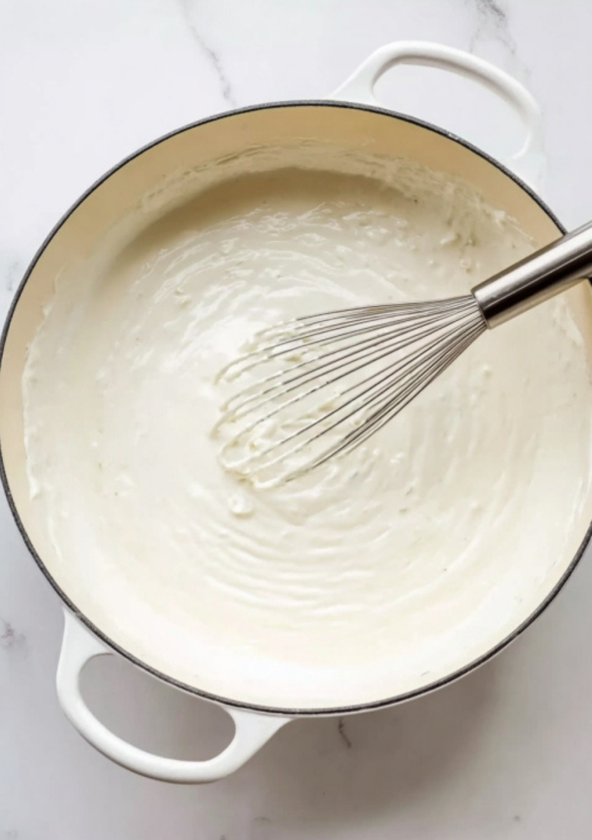 Smooth white sauce being whisked in a Dutch oven, ready to become the base of a cheesy spinach artichoke pasta bake.