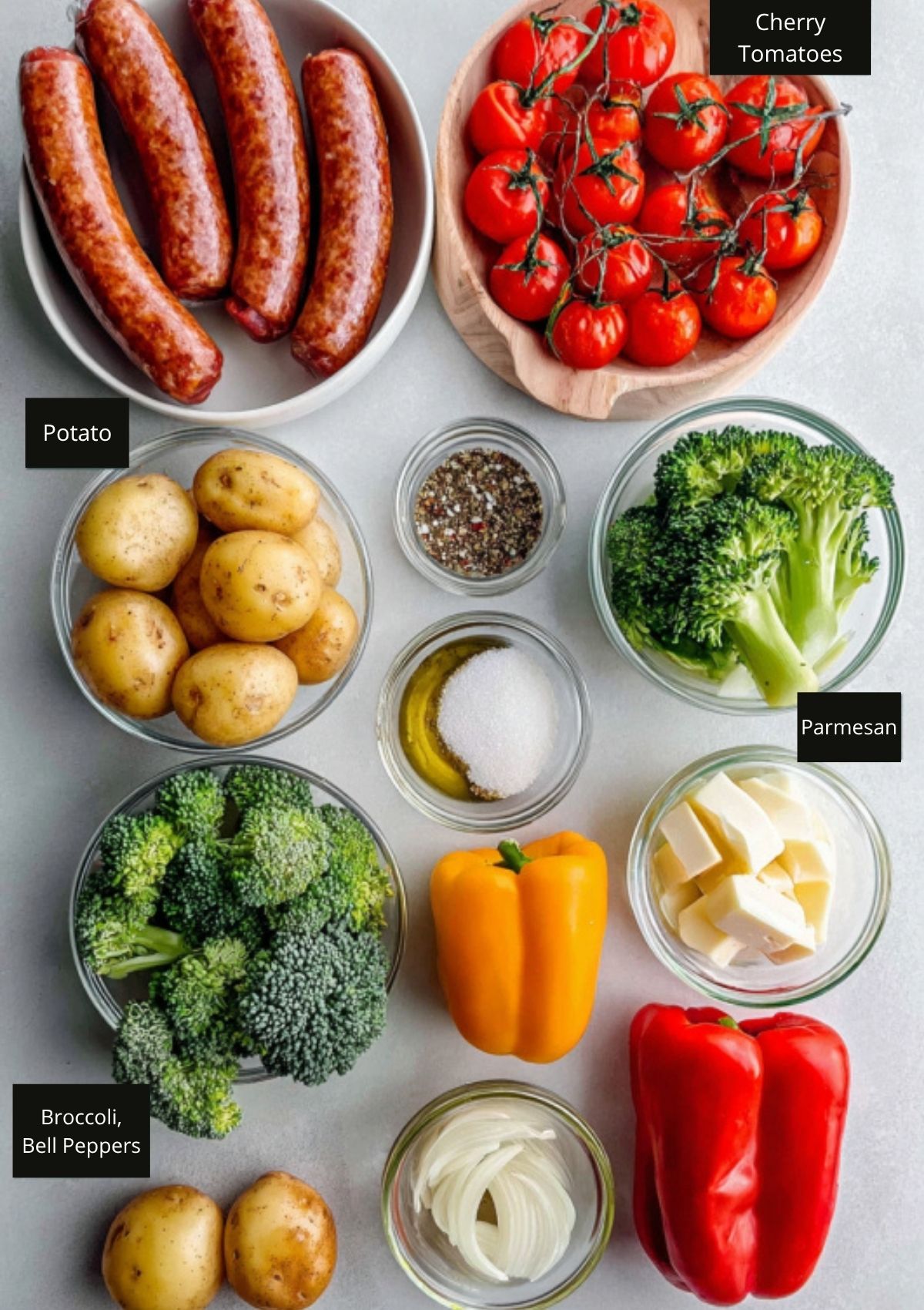 Assorted fresh ingredients for sheet-pan sausage and veggies including sausage links, potatoes, broccoli, bell peppers, olive oil, and seasonings.