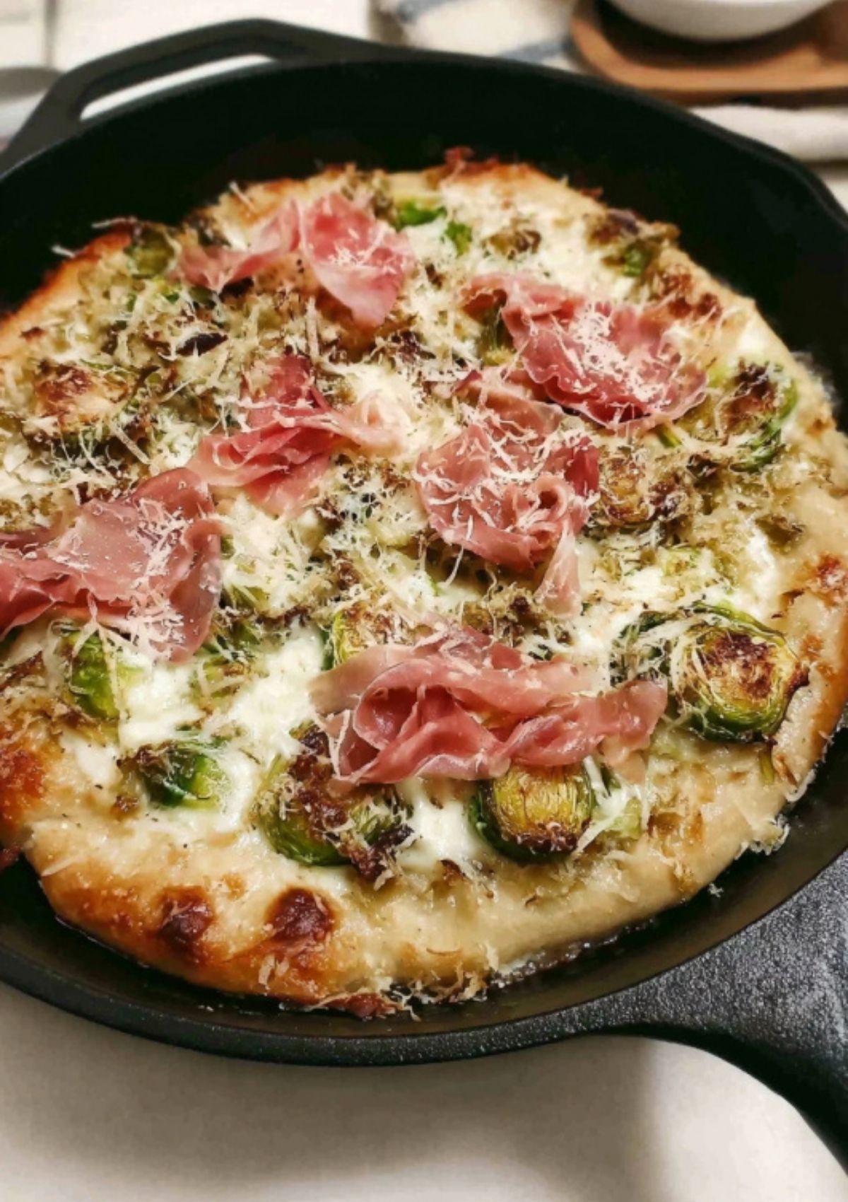 Golden baked pizza topped with crispy prosciutto, roasted Brussels sprouts, and melted cheese in a skillet.