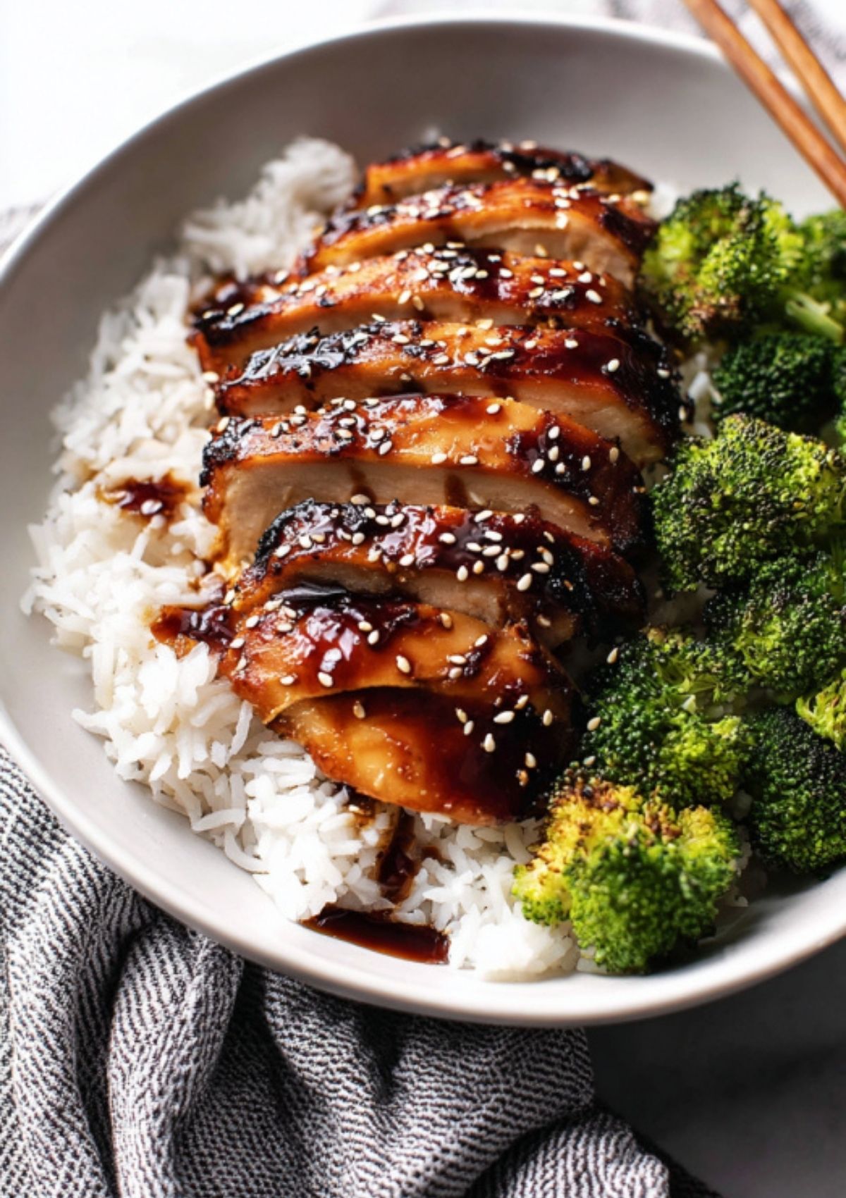 Sliced teriyaki chicken glazed with sauce, served over fluffy white rice with roasted broccoli and sesame seeds.