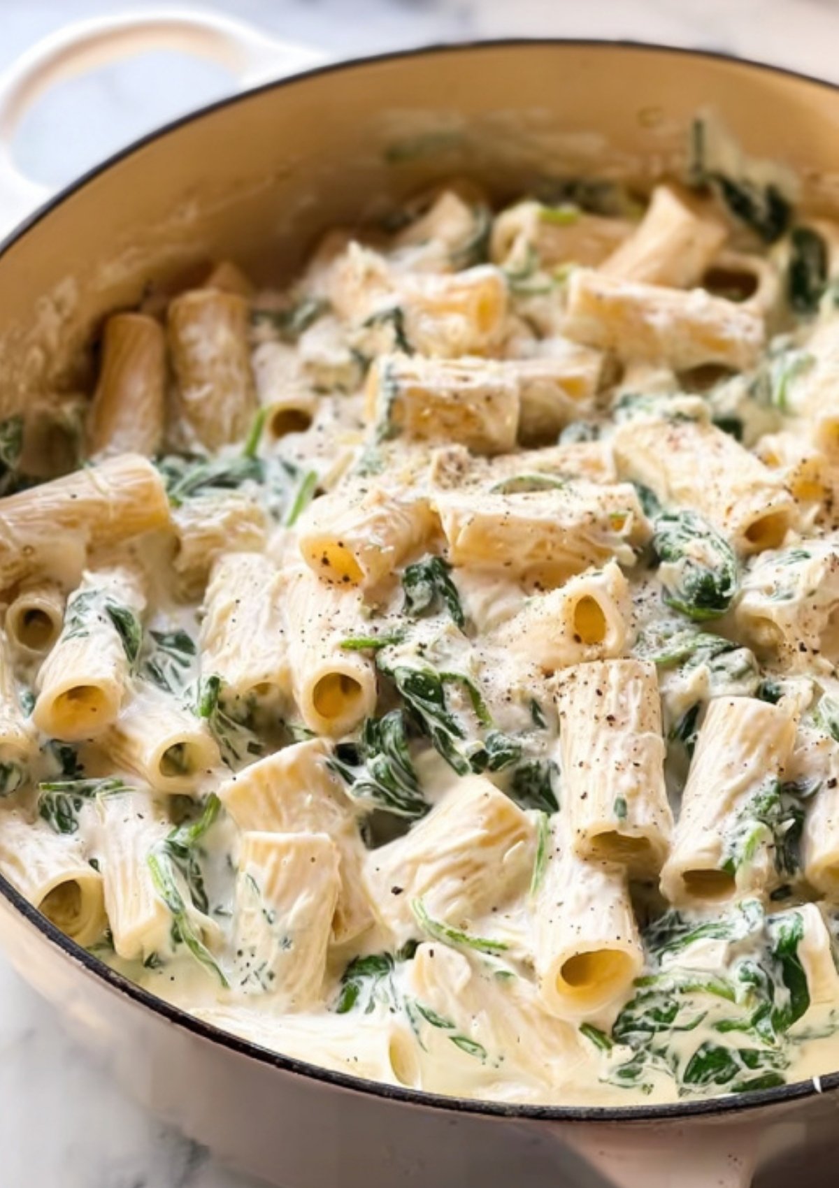 Rigatoni pasta mixed with spinach and artichoke in a rich, creamy cheese sauce, ready to bake.