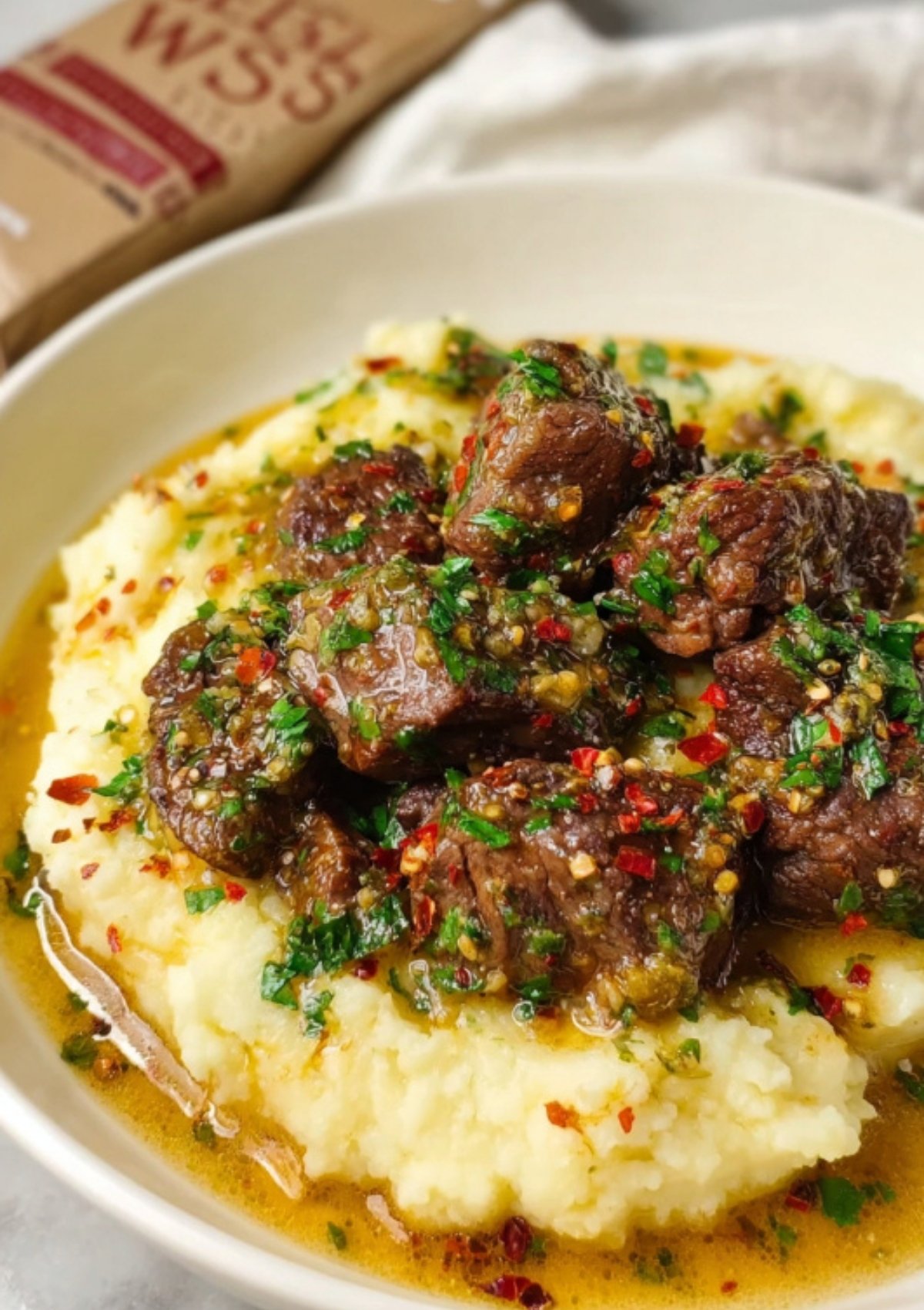 Juicy garlic butter steak bites served over creamy mashed potatoes, topped with fresh herbs, red pepper flakes, and melted butter sauce.