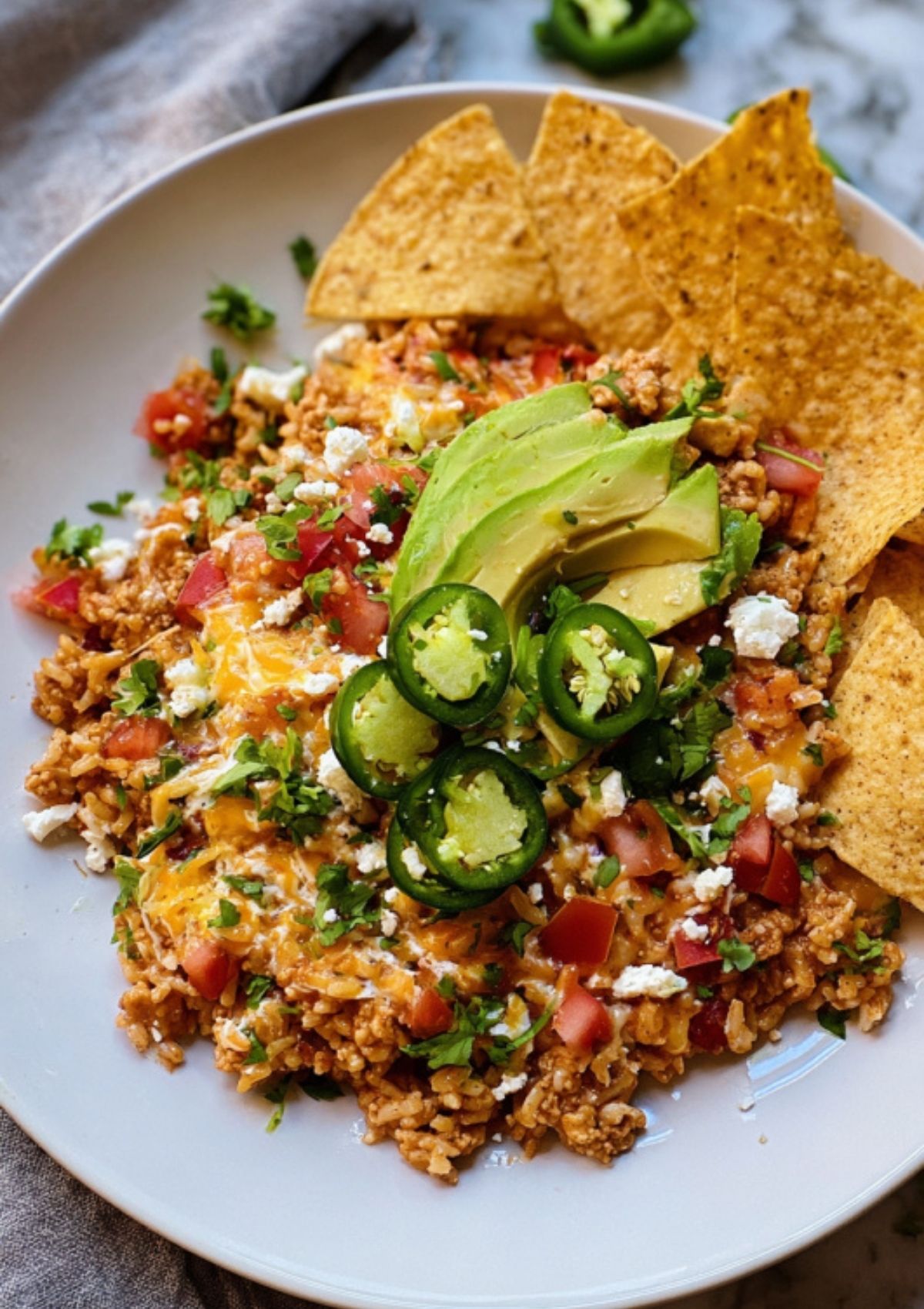 Bowl of cheesy turkey taco skillet topped with avocado, jalapeños, fresh cilantro, and tortilla chips for serving.