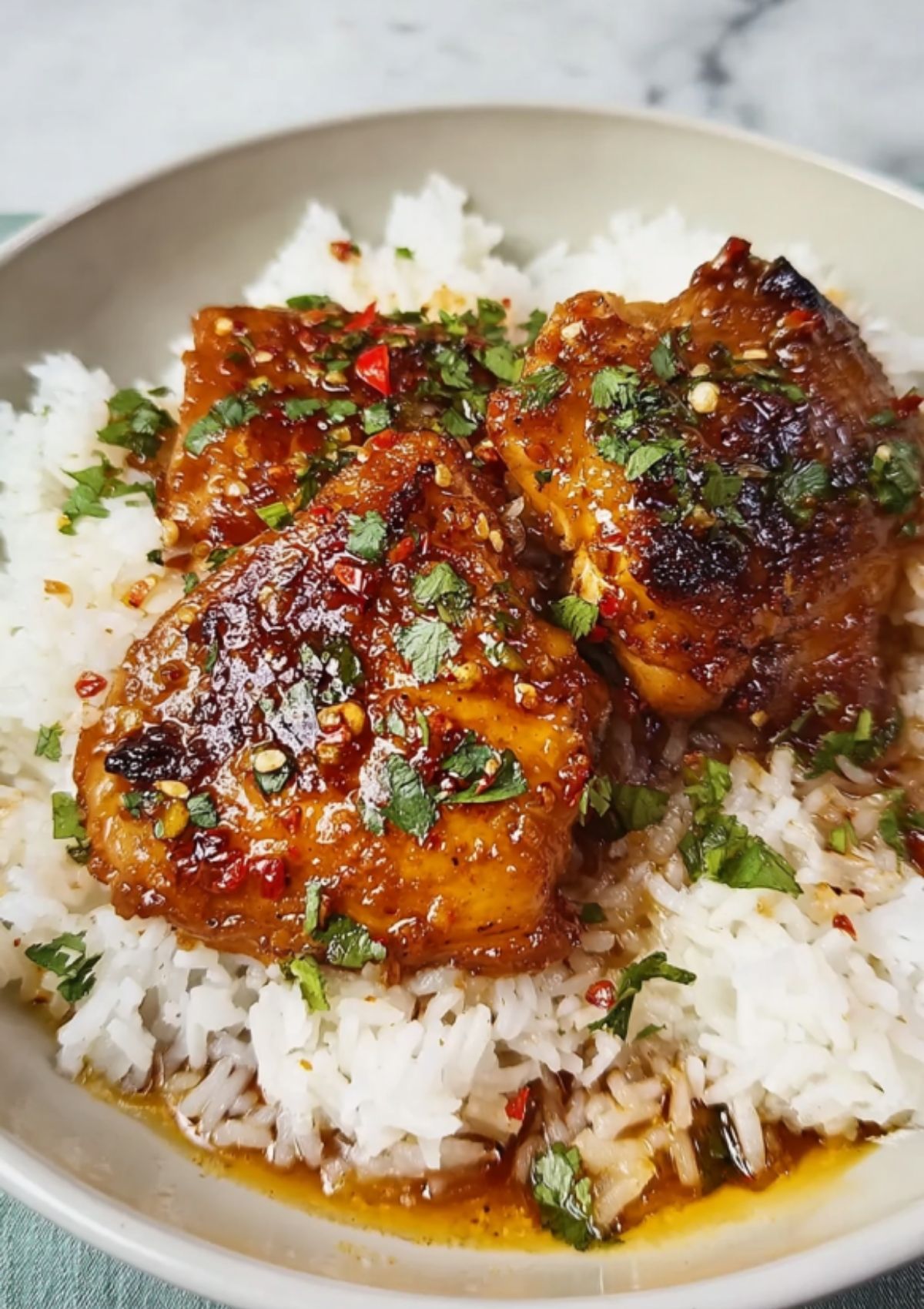 Three sticky honey garlic chicken thighs served over fluffy white rice, garnished with fresh cilantro and chili flakes.