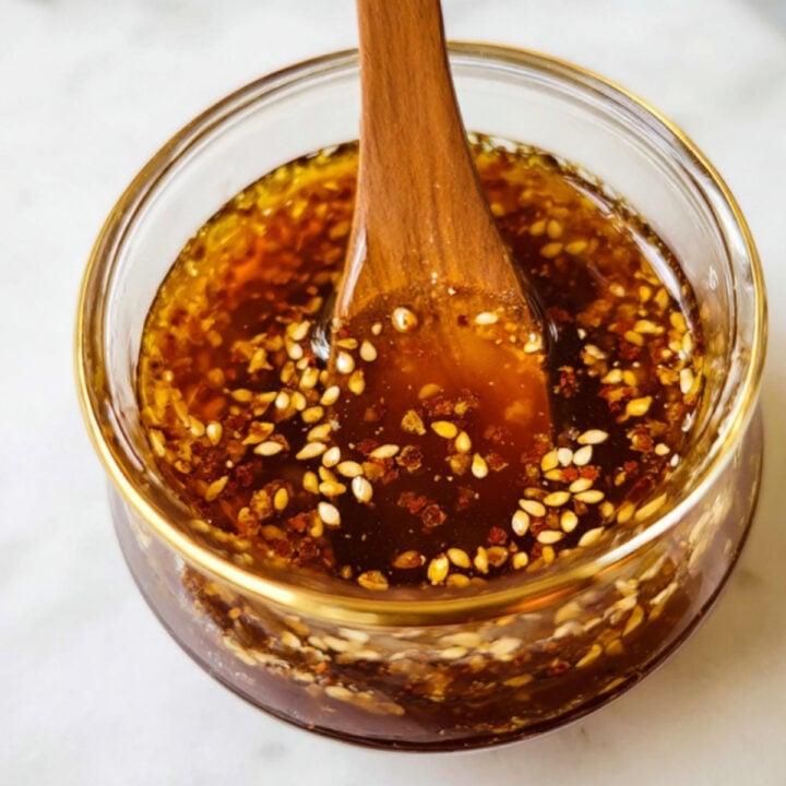 Close up of soy ginger sauce with sesame seeds in a glass jar and wooden spoon. Perfect for stir fry, Asian bowls, marinades, and healthy meal prep.