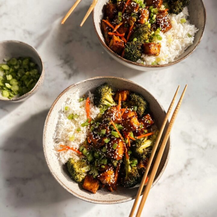 Two bowls filled with tofu stir-fry, broccoli, carrots, and white rice, topped with green onions and sesame seeds. Perfect for healthy vegan meal prep and plant-based dinner ideas.