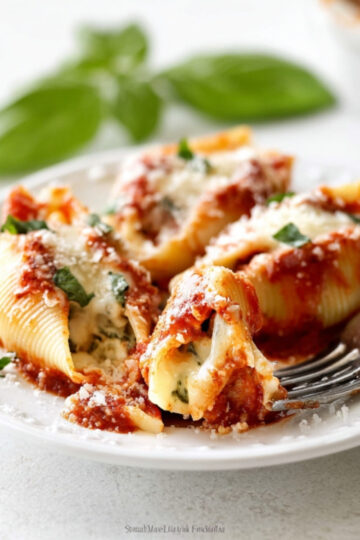 Serving plate with cheesy chicken and spinach stuffed shells, topped with extra Parmesan, basil, and tomato sauce.