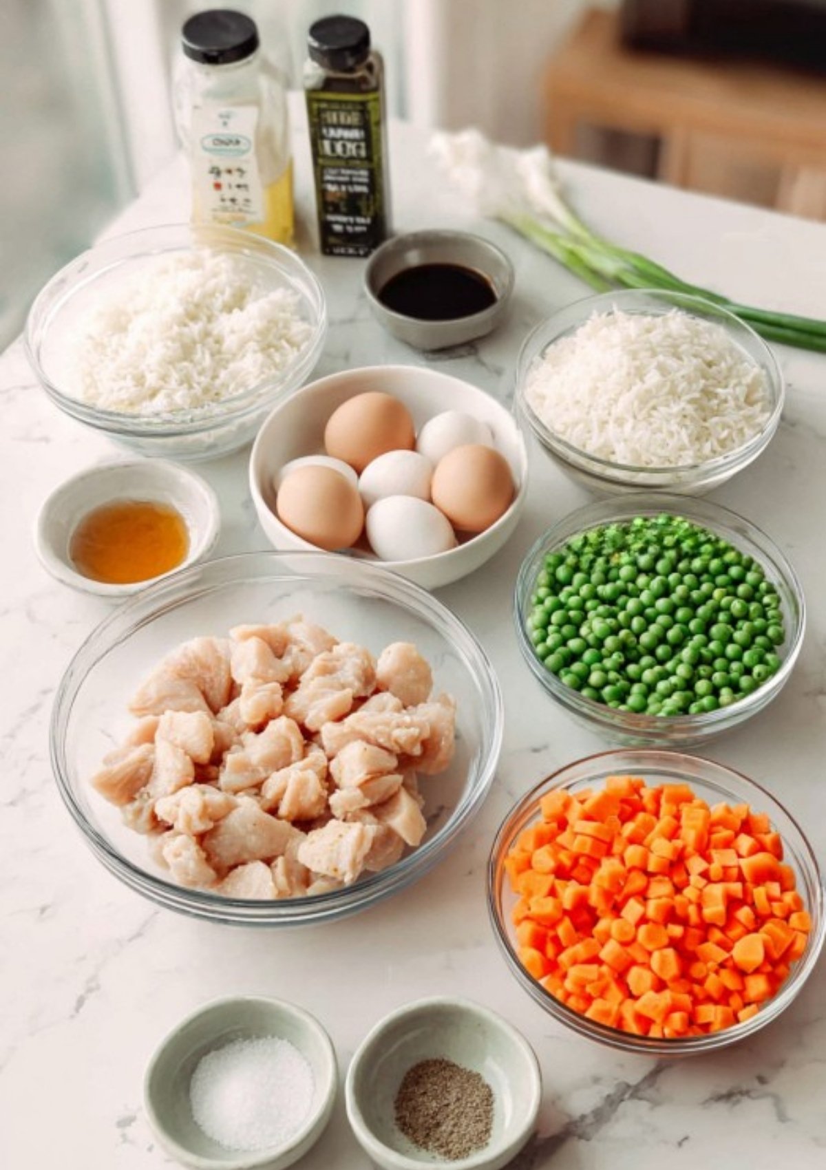 All the ingredients for chicken fried rice—chicken, rice, eggs, peas, carrots, soy sauce—prepped in bowls.