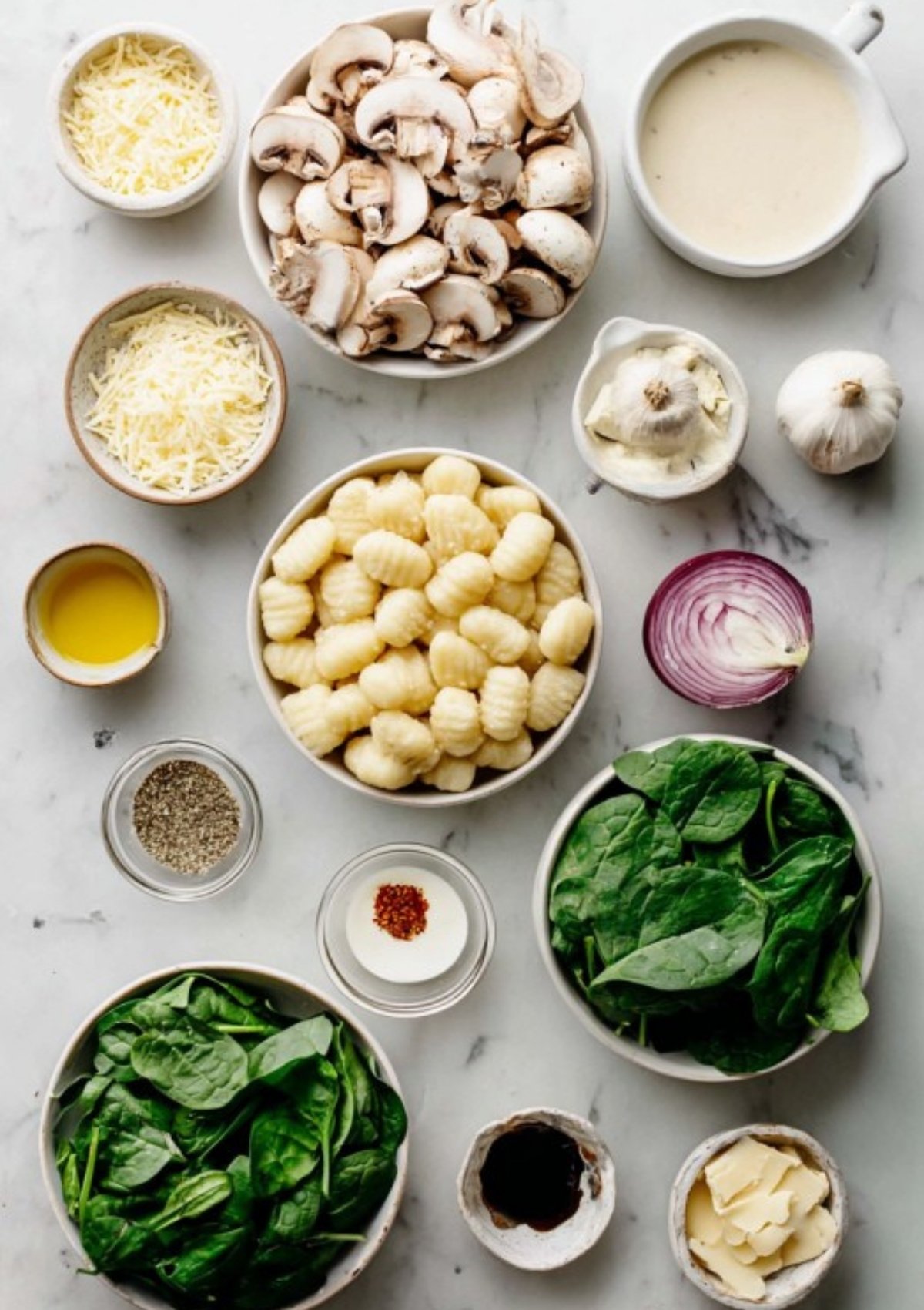 Overhead shot of fresh ingredients for creamy mushroom gnocchi, including spinach, mushrooms, gnocchi, heavy cream, Parmesan, onion, and garlic.