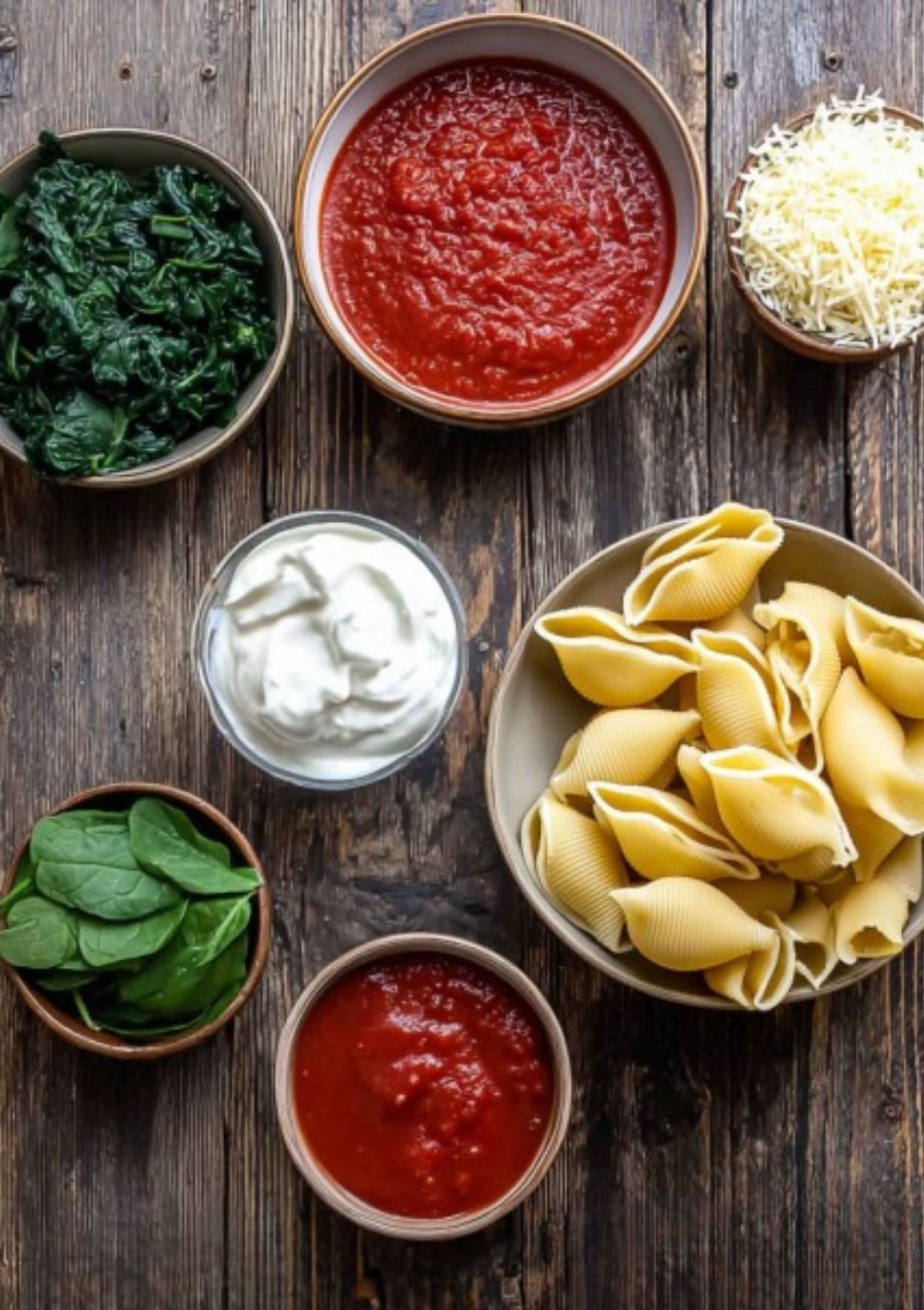 Flat lay of ingredients for chicken and spinach stuffed shells, including jumbo pasta shells, spinach, marinara, shredded cheese, and Greek yogurt.