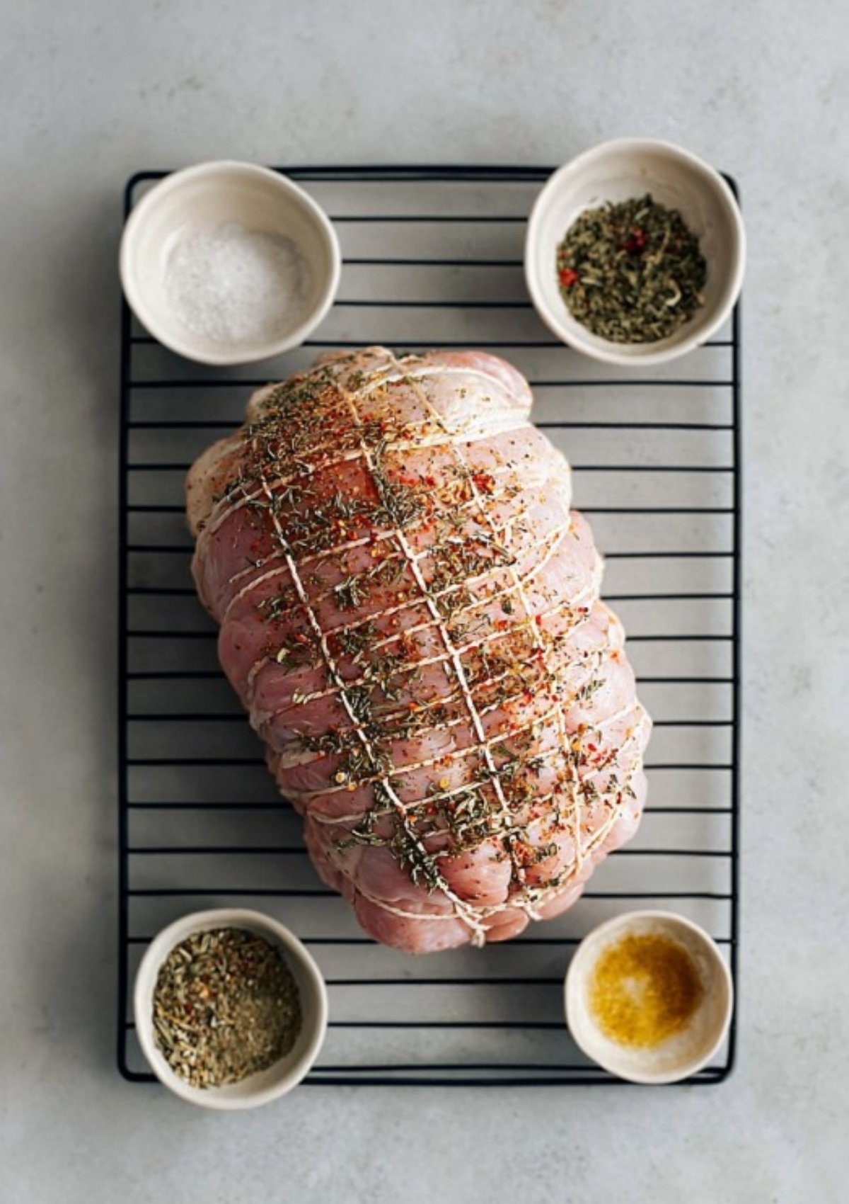 Uncooked Butterball turkey breast roast tied with twine and seasoned, surrounded by bowls of spices.