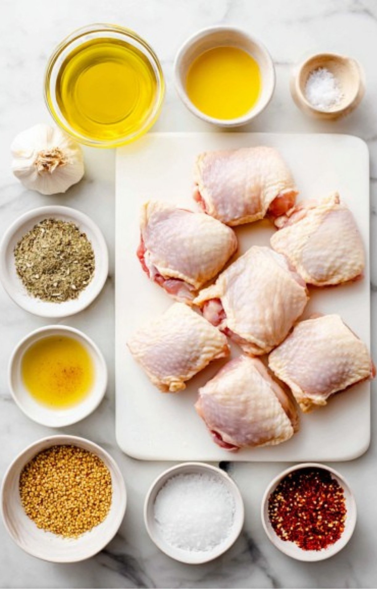 Chicken thighs, olive oil, garlic, mustard, honey, and seasonings arranged on white cutting board for easy baked chicken