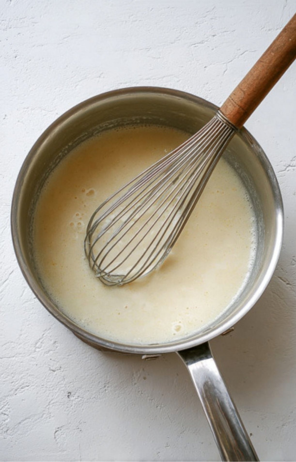 Smooth homemade cheese sauce in a saucepan with a whisk, ready to pour over roast beef sandwiches