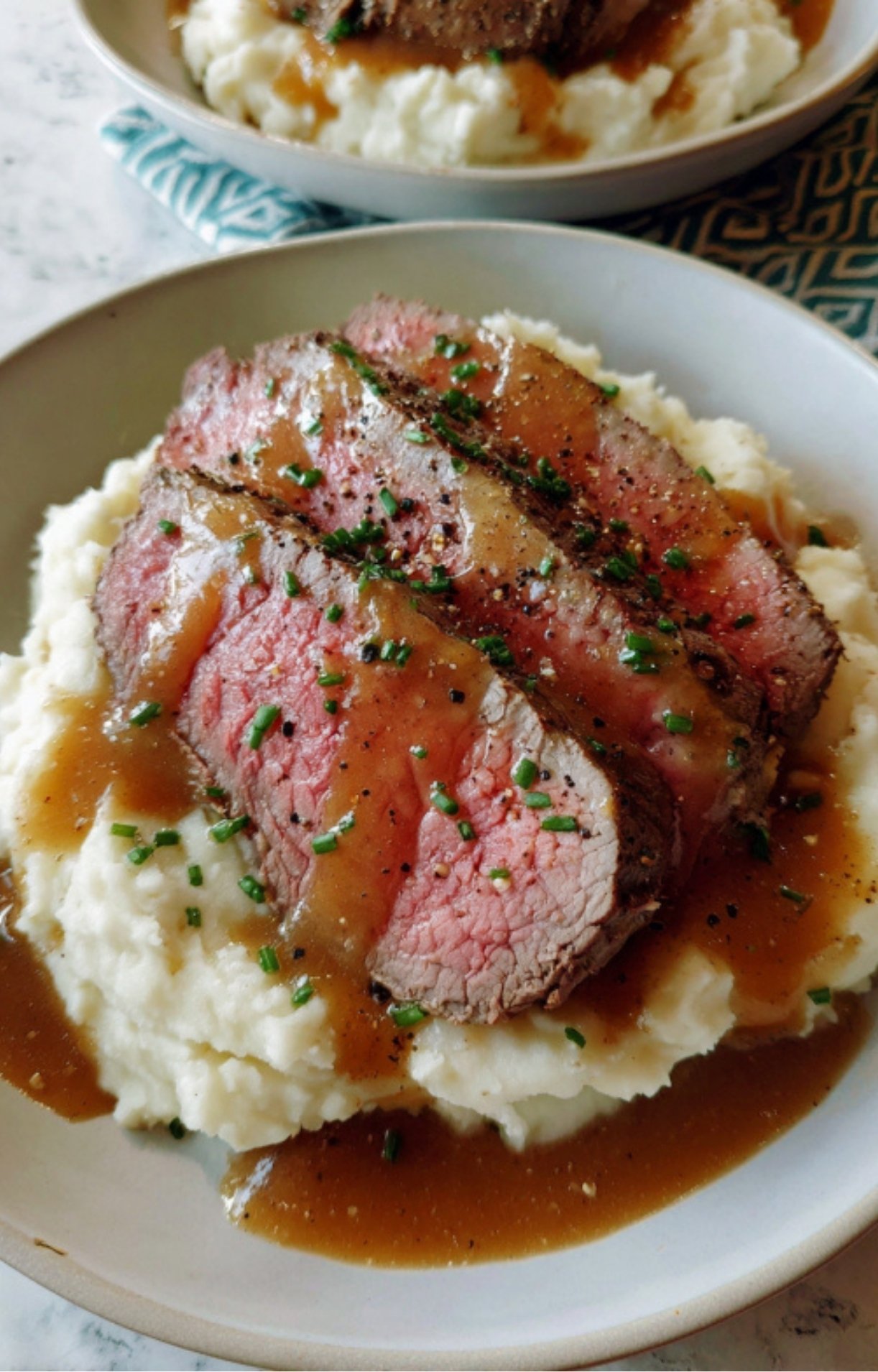 Sliced beef roast served over creamy mashed potatoes and topped with homemade brown gravy and chives