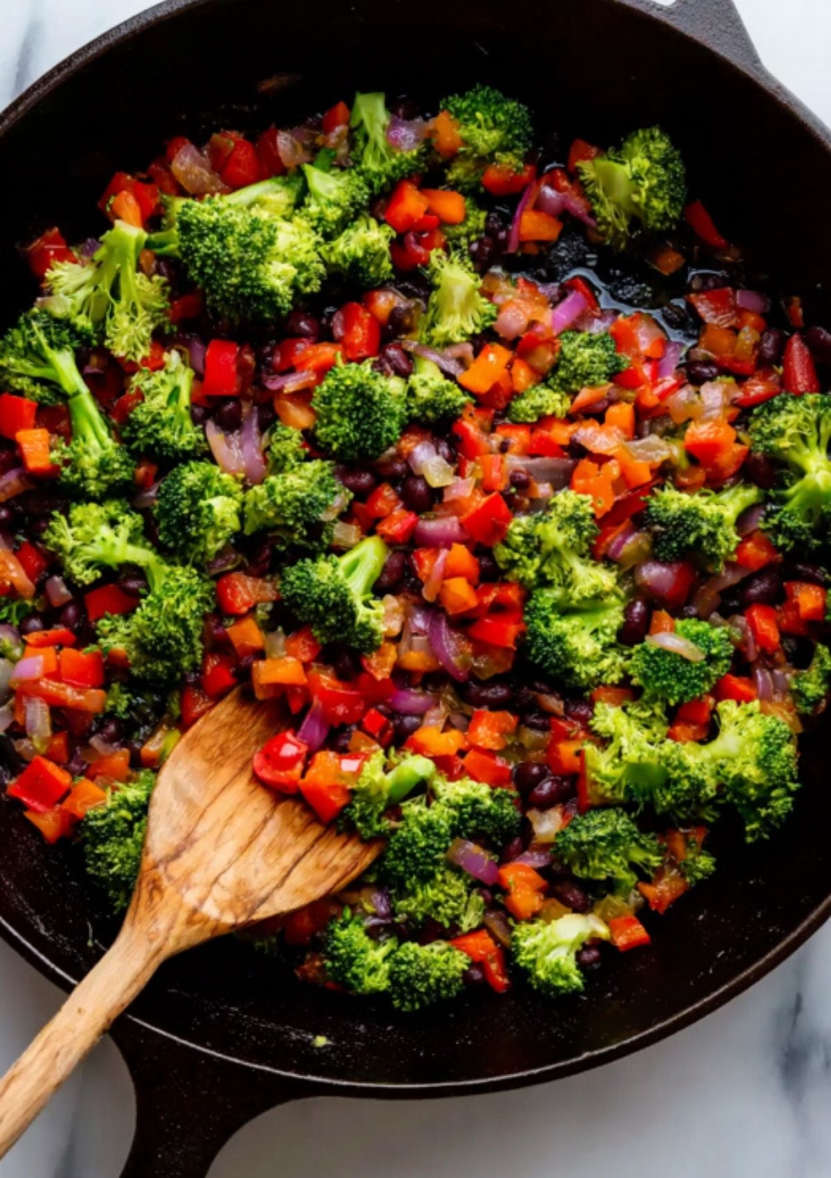 Sautéed broccoli, red bell pepper, onion, and black beans in a cast iron skillet – easy step for vegetarian black bean enchilada filling.