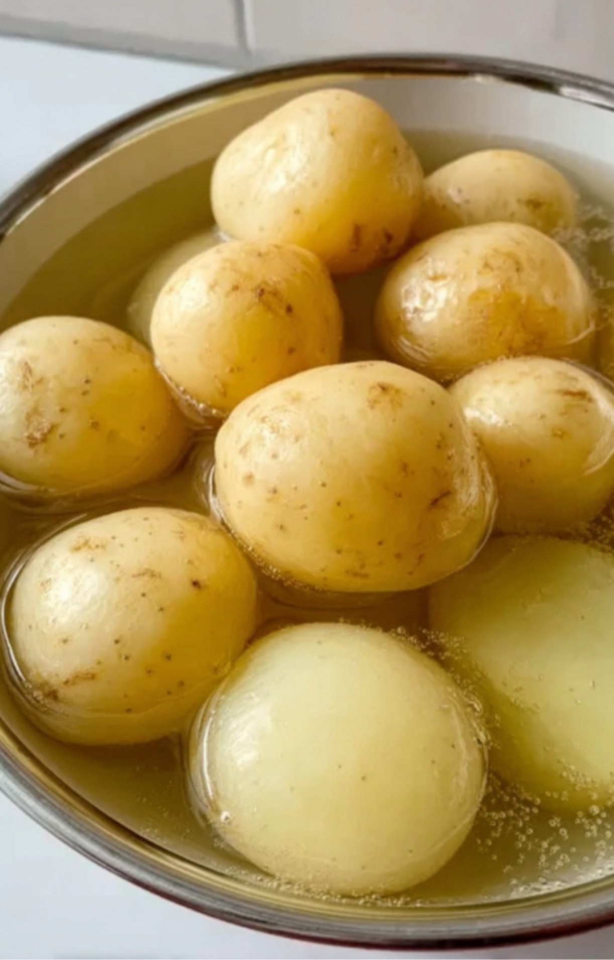 Bowl of whole baby potatoes submerged in water, ready to be parboiled as the secret step for perfectly crispy roasted potatoes.