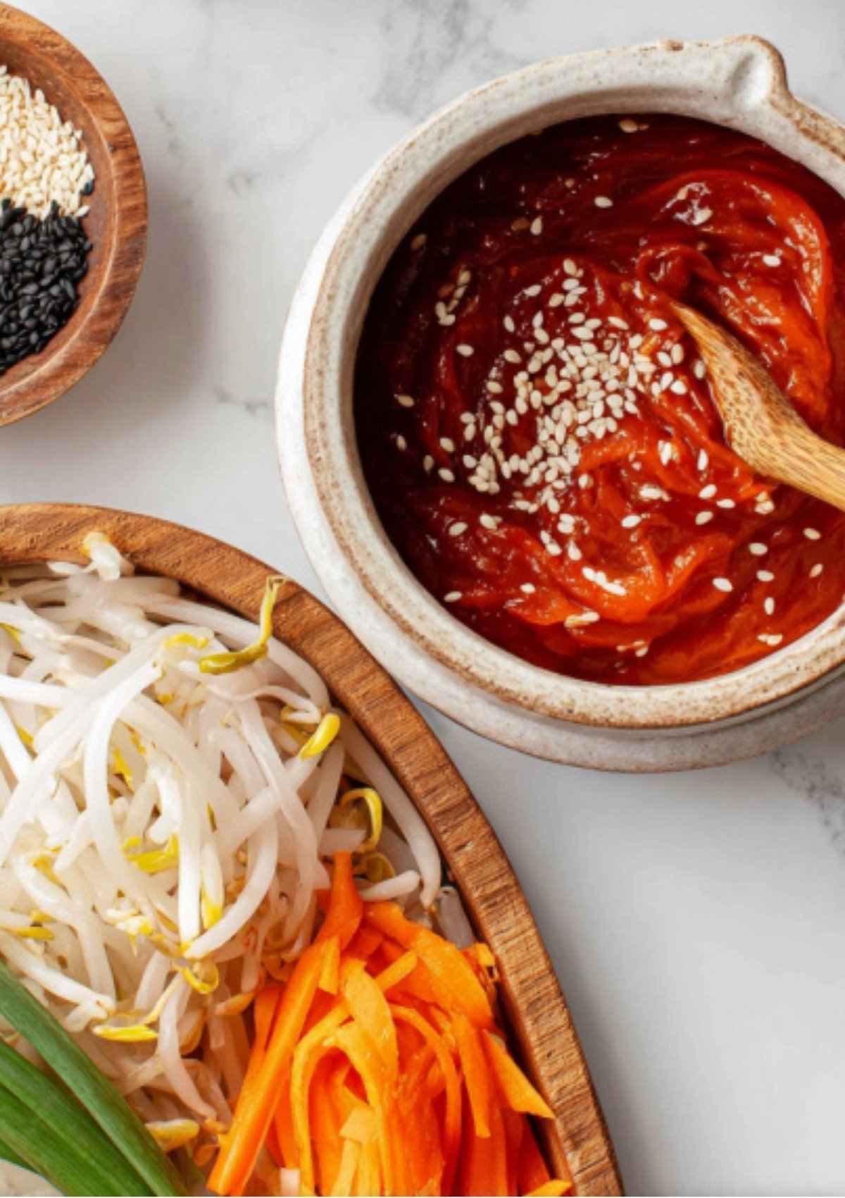 Ceramic bowl of gochujang sauce with sesame seeds, bean sprouts, and shredded carrots