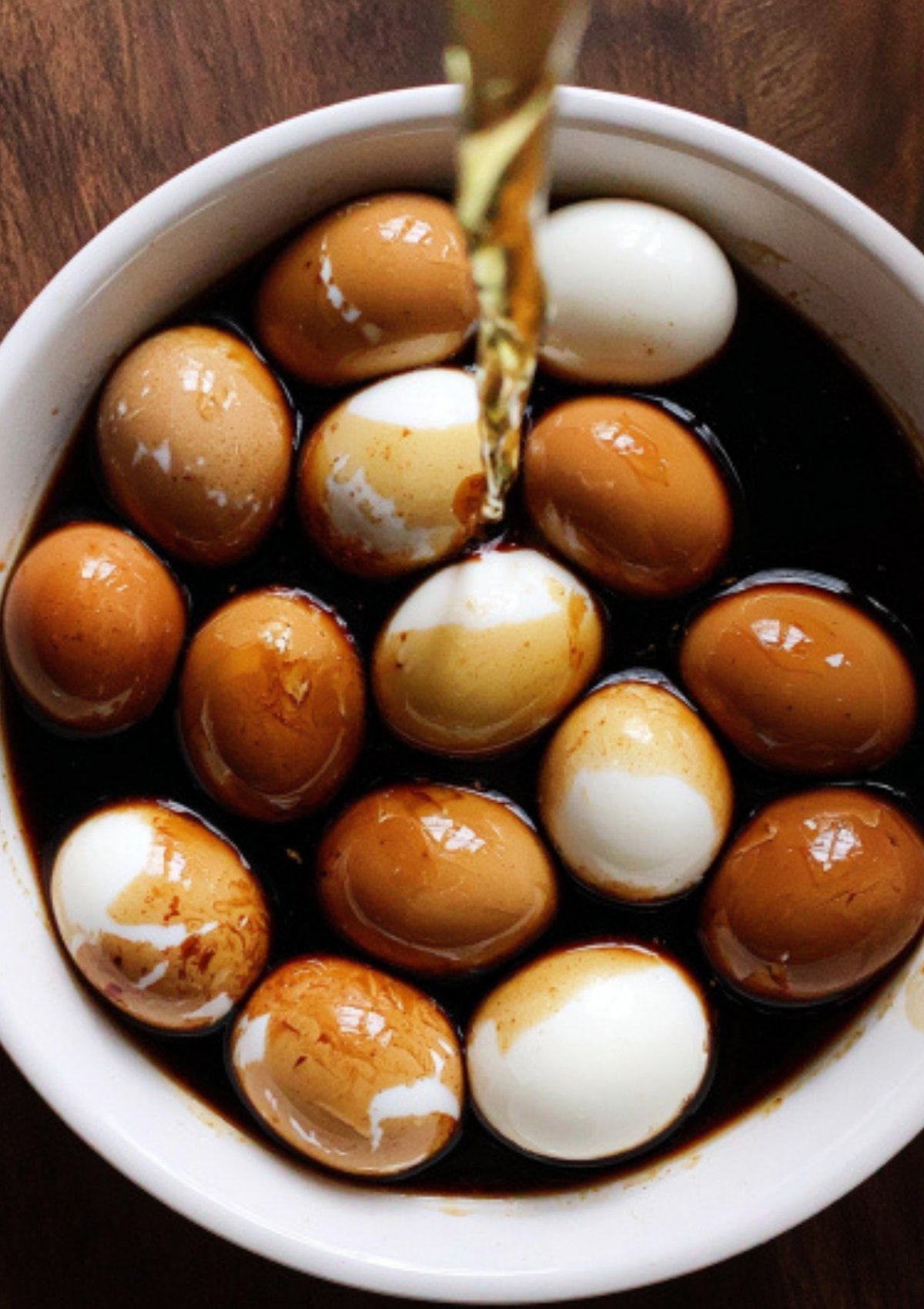 Whole hard-boiled eggs being marinated in a bowl of soy sauce mixture, some eggs partially peeled.