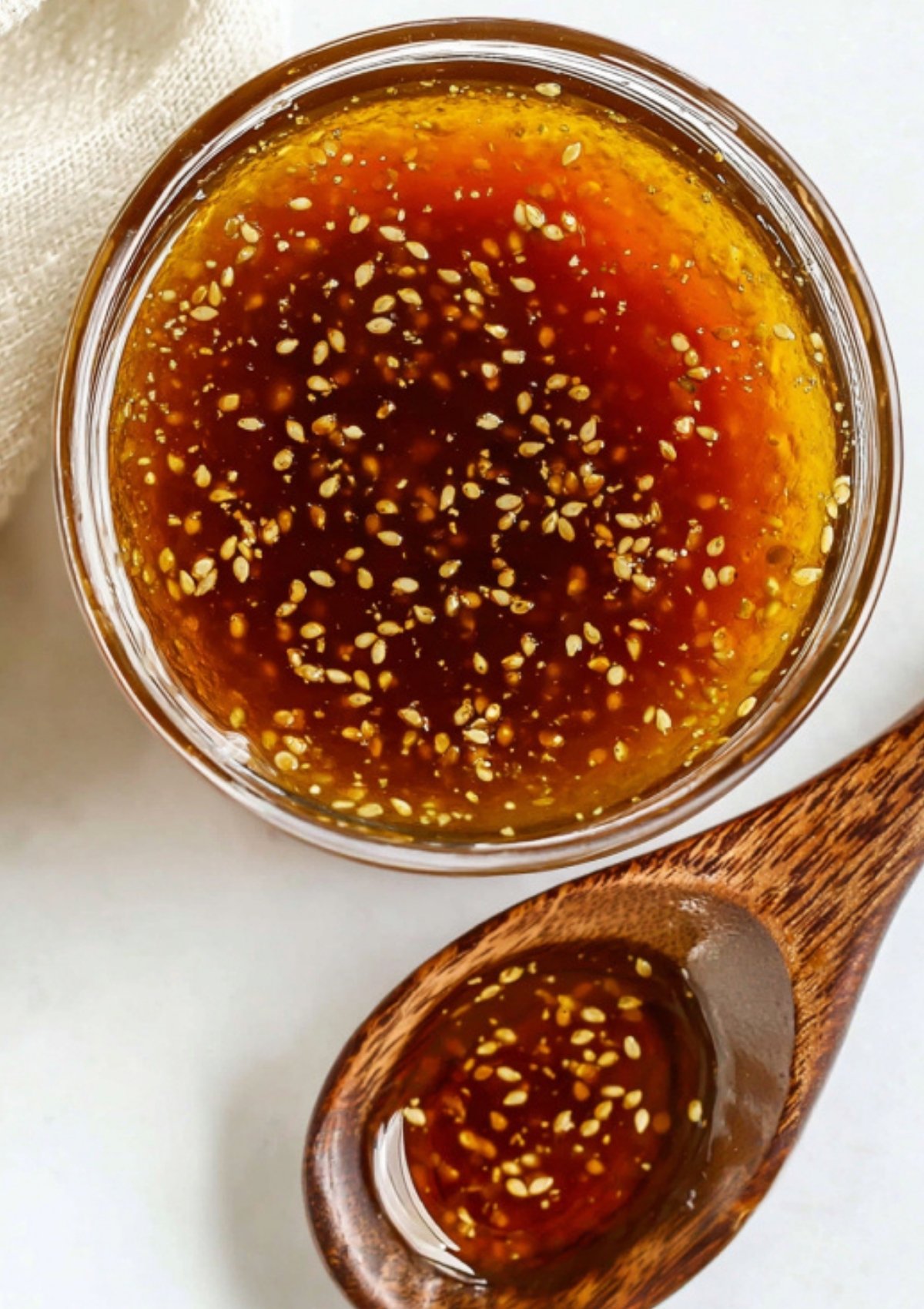 Top view of soy ginger sauce with sesame seeds in a glass bowl and wooden spoon. Quick homemade sauce for salads, bowls, and noodle dishes.
