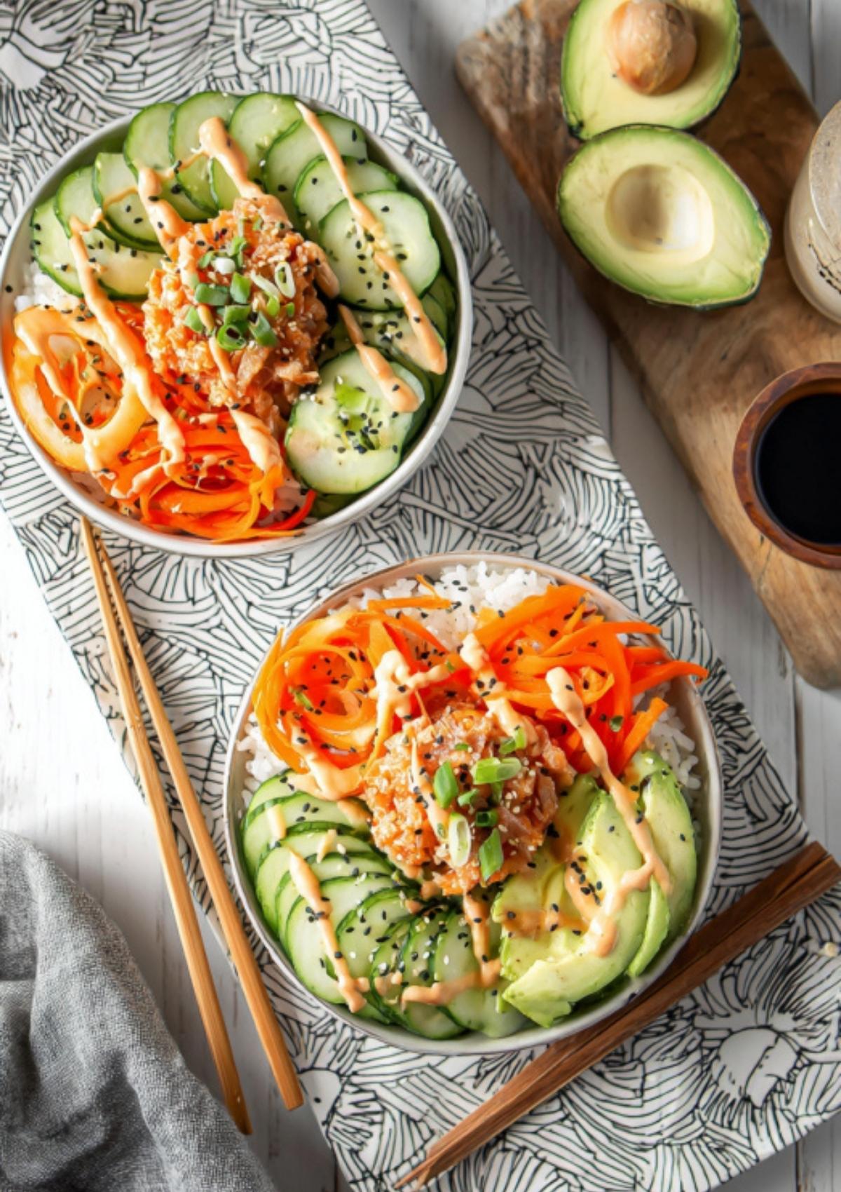 Two colorful spicy tuna rice bowls with avocado, cucumber, carrots, rice, and spicy mayo drizzle.