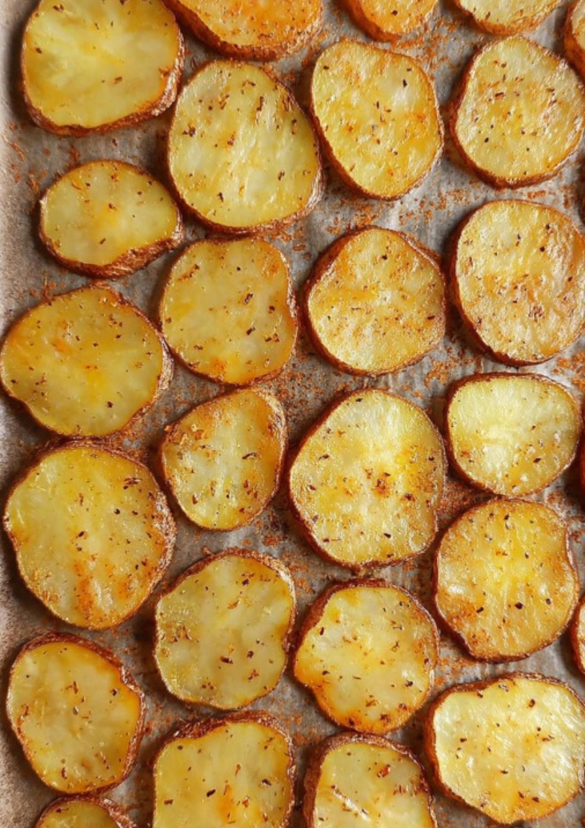 Raw potato slices arranged on a baking tray, seasoned with spices and olive oil, ready to be roasted.