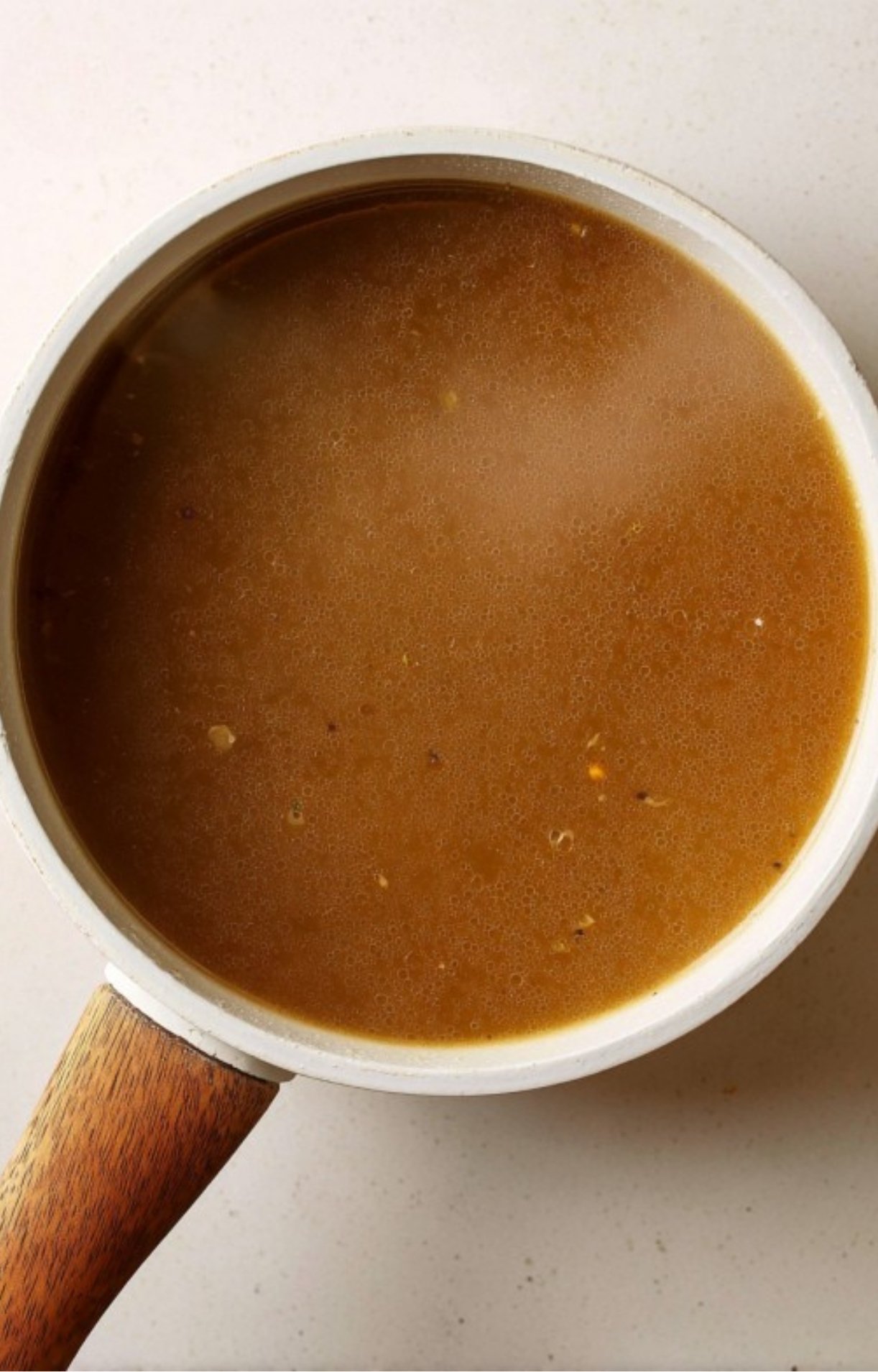 Pot of smooth, homemade brown gravy on a white countertop, ready for serving with classic beef roast