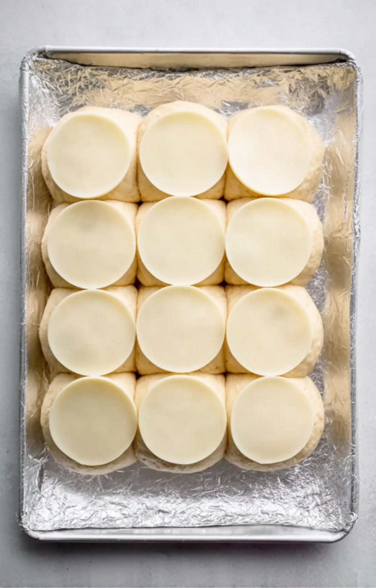 Unbaked slider rolls topped with provolone cheese slices, assembled on a tray for fast and easy baked sliders.
