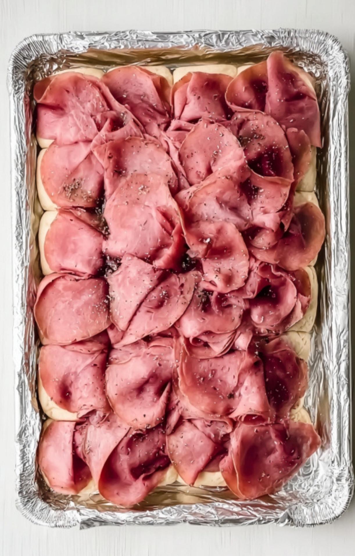 Fluffy slider buns topped with layers of deli roast beef, ready to be baked for a quick and tasty appetizer.