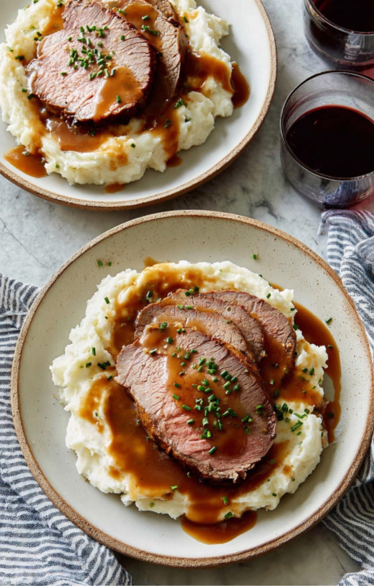 Plates of sliced roast beef with brown gravy over mashed potatoes, served with red wine