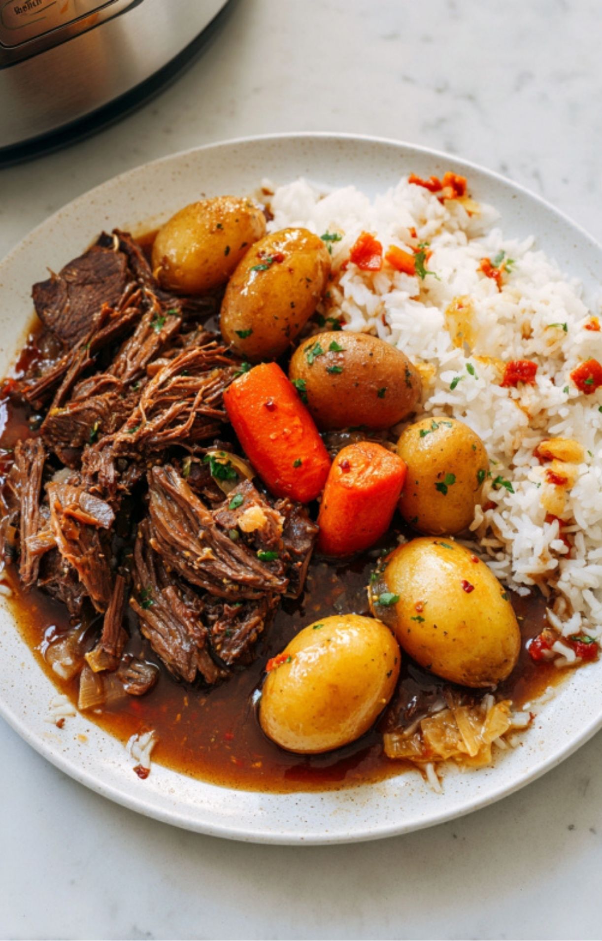 Shredded pot roast served with baby potatoes, carrots, and a side of white rice on a plate