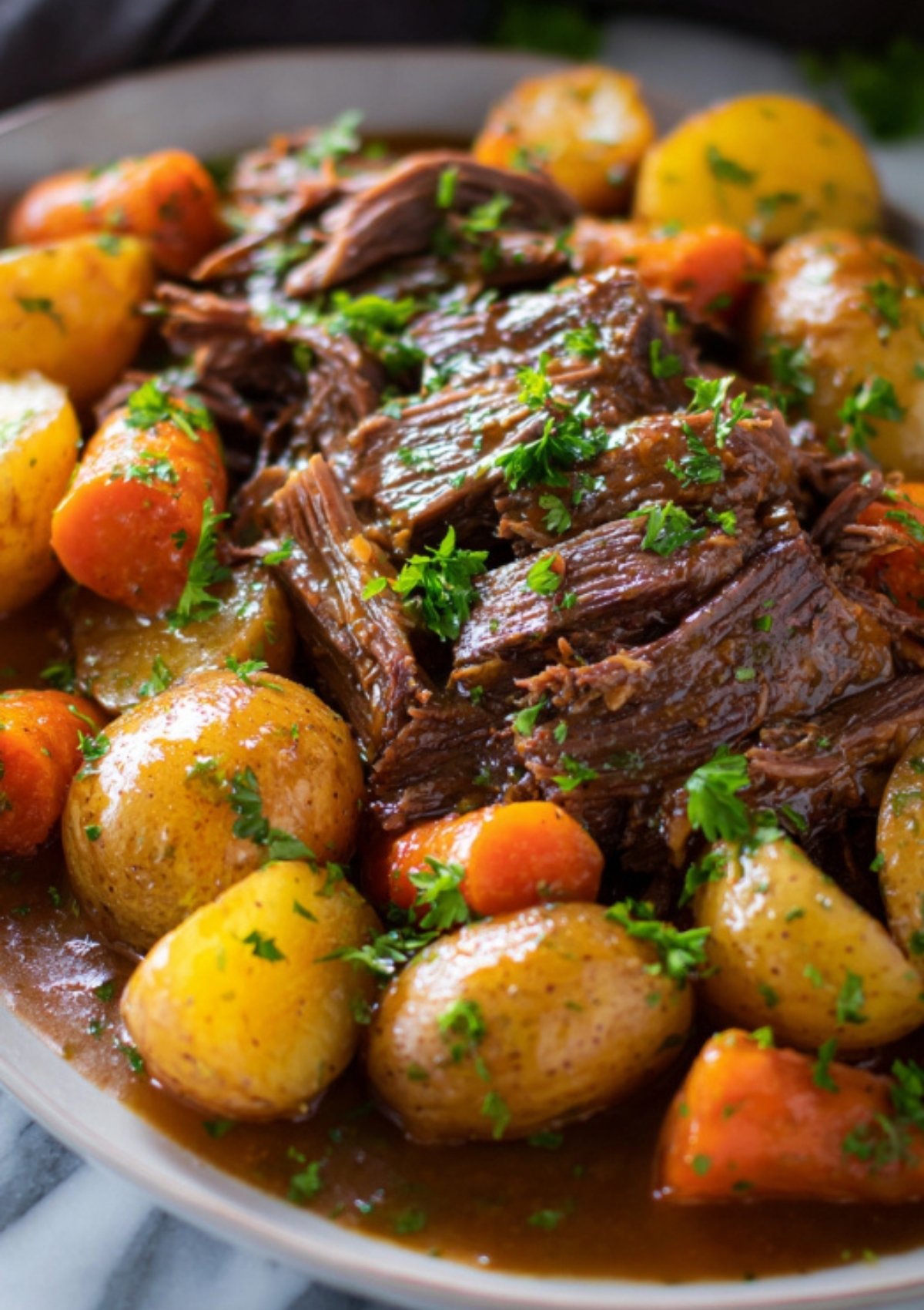 Close-up of fork-tender beef pot roast with carrots and potatoes, topped with fresh herbs.