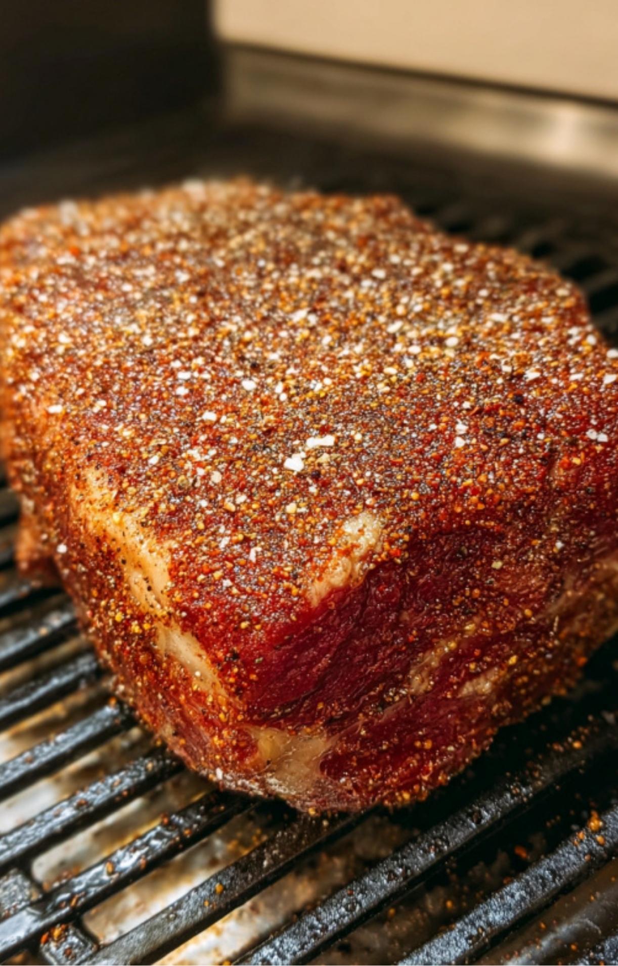 Beef chuck roast coated in a dry spice rub, sitting on a smoker rack ready to be slow cooked for juicy BBQ flavor