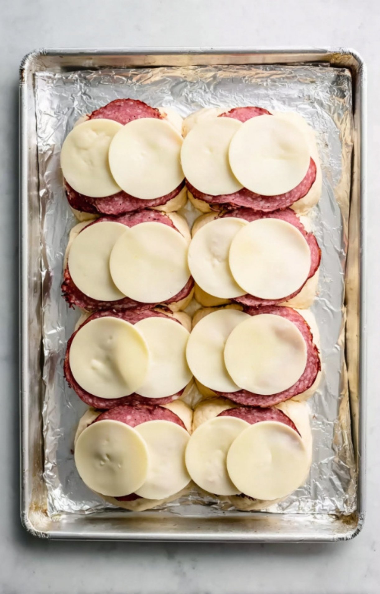 Sliced roast beef and provolone cheese layered on slider buns, prepped on a baking sheet for easy oven-baked sliders.