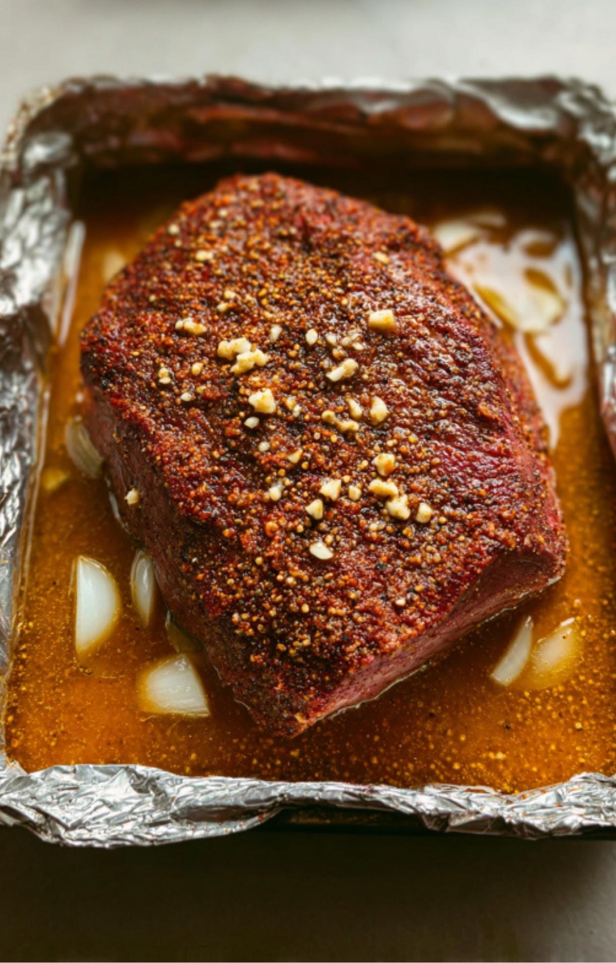 Chuck roast braising in a foil pan with onions and broth, ready for smoking or oven roasting