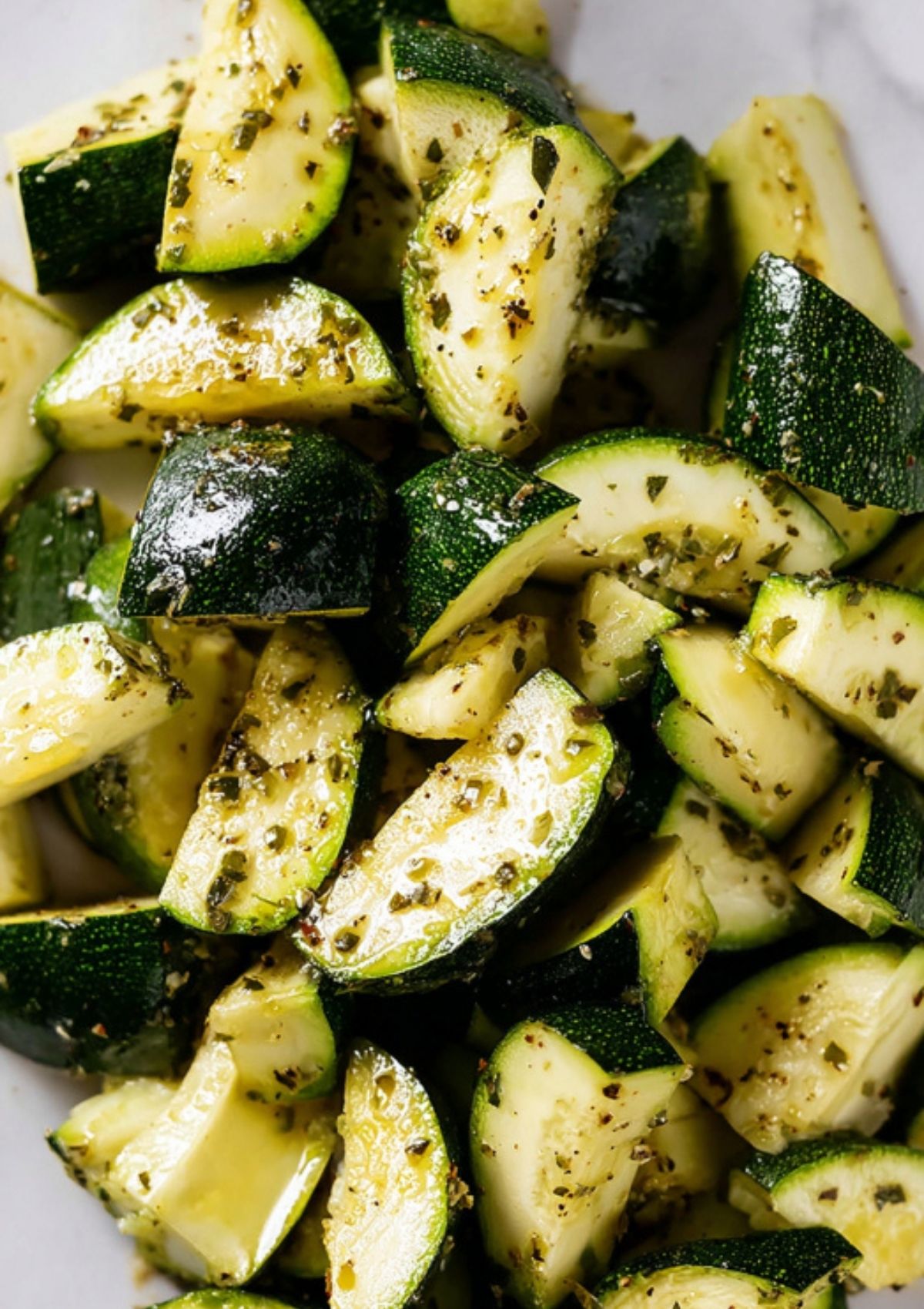 Bowl of zucchini pieces coated in olive oil and herbs, ready for roasting.