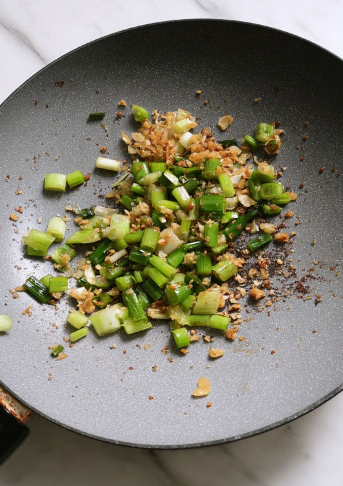 Green onions and crispy garlic sizzling in a wok, creating the base for flavorful soy sauce noodles.